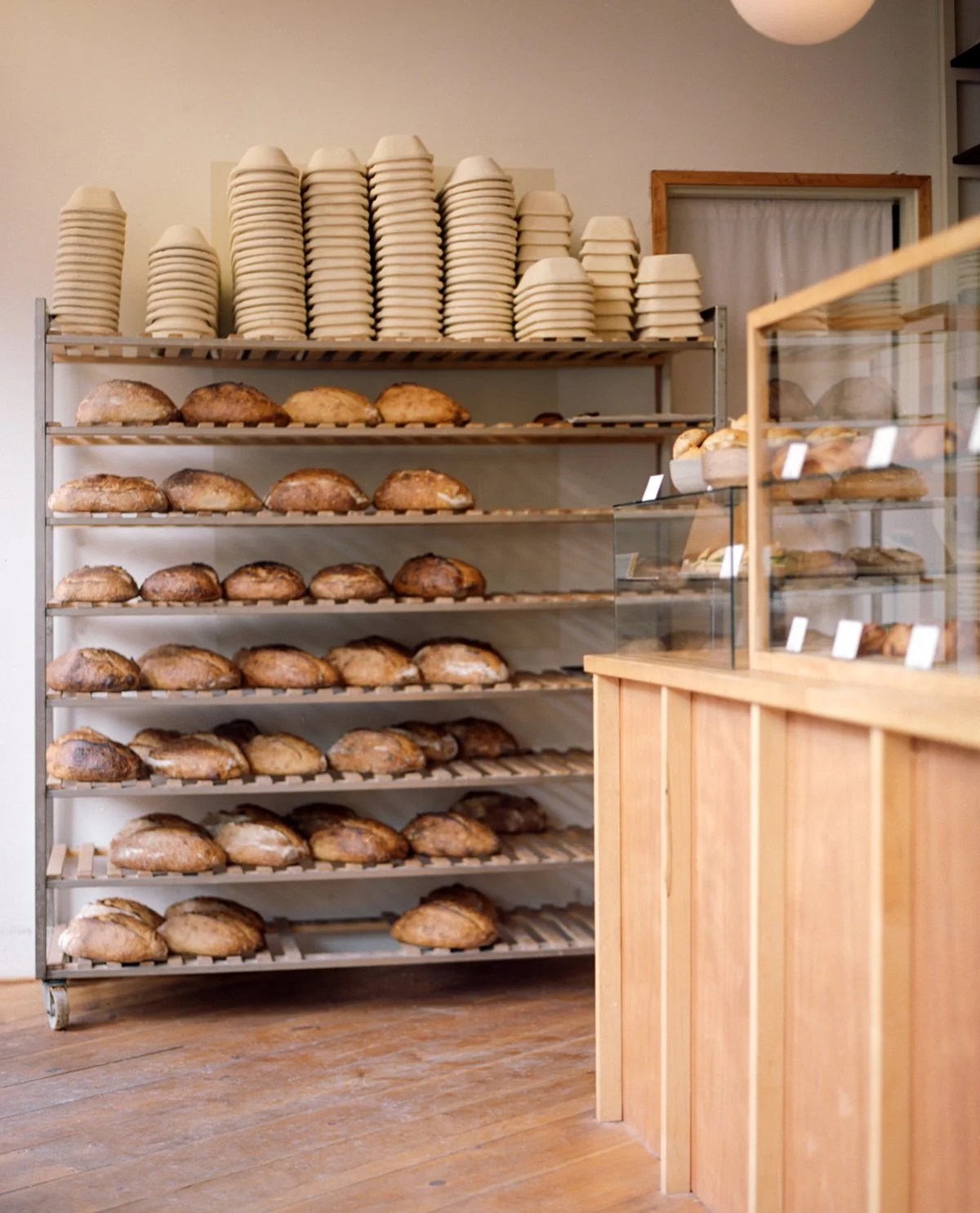 A bakery display with shelves of bread and a counter with pastries, with the bread on metal racks and pastries in a wooden display case.