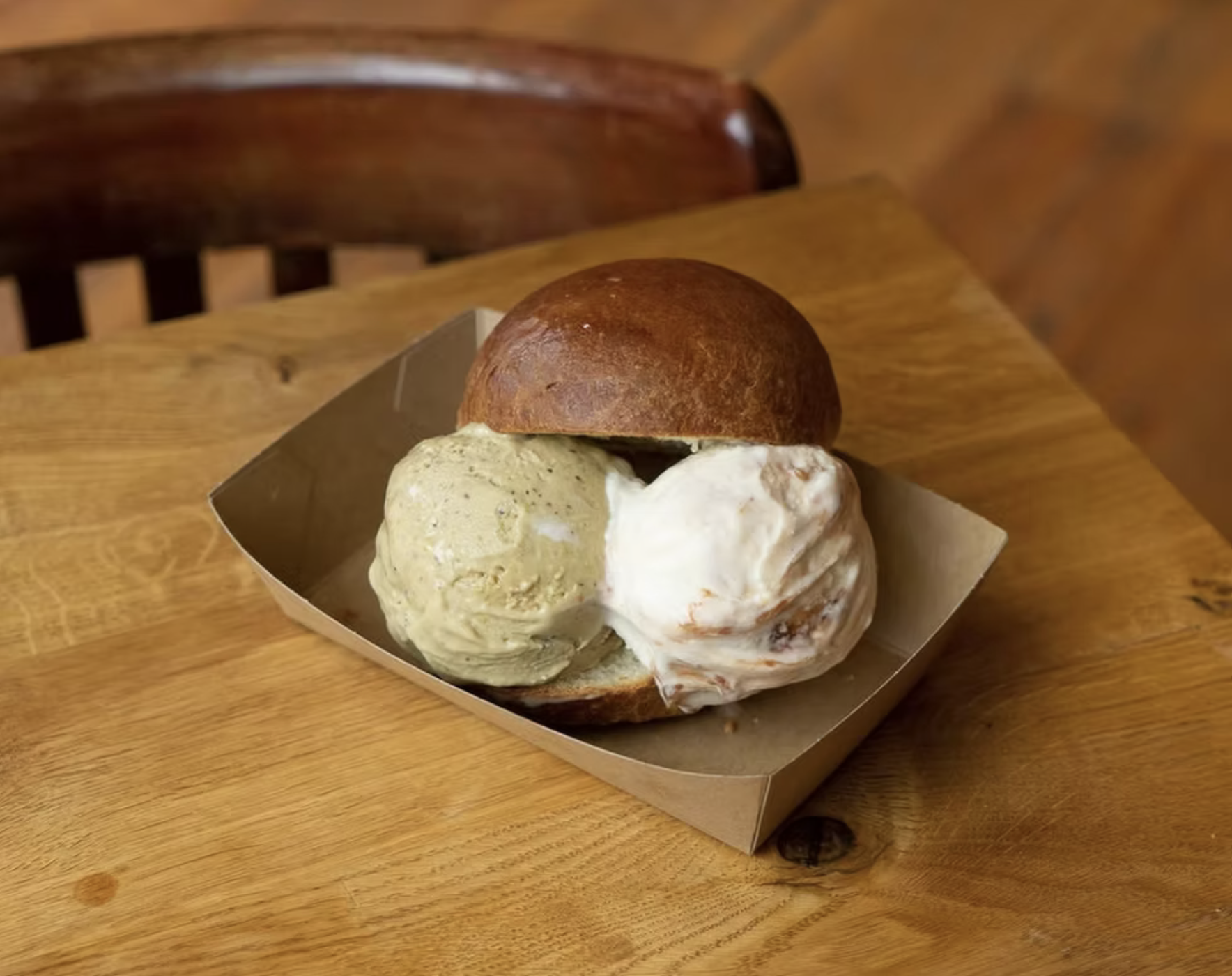 A dessert sandwich with two scoops of ice cream in a bun, served on a small tray on a wooden table.