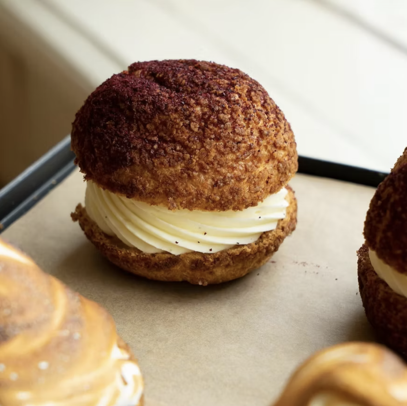 A close-up of a dessert device with a crunchy exterior, filled with whipped cream, on a parchment paper-lined tray.