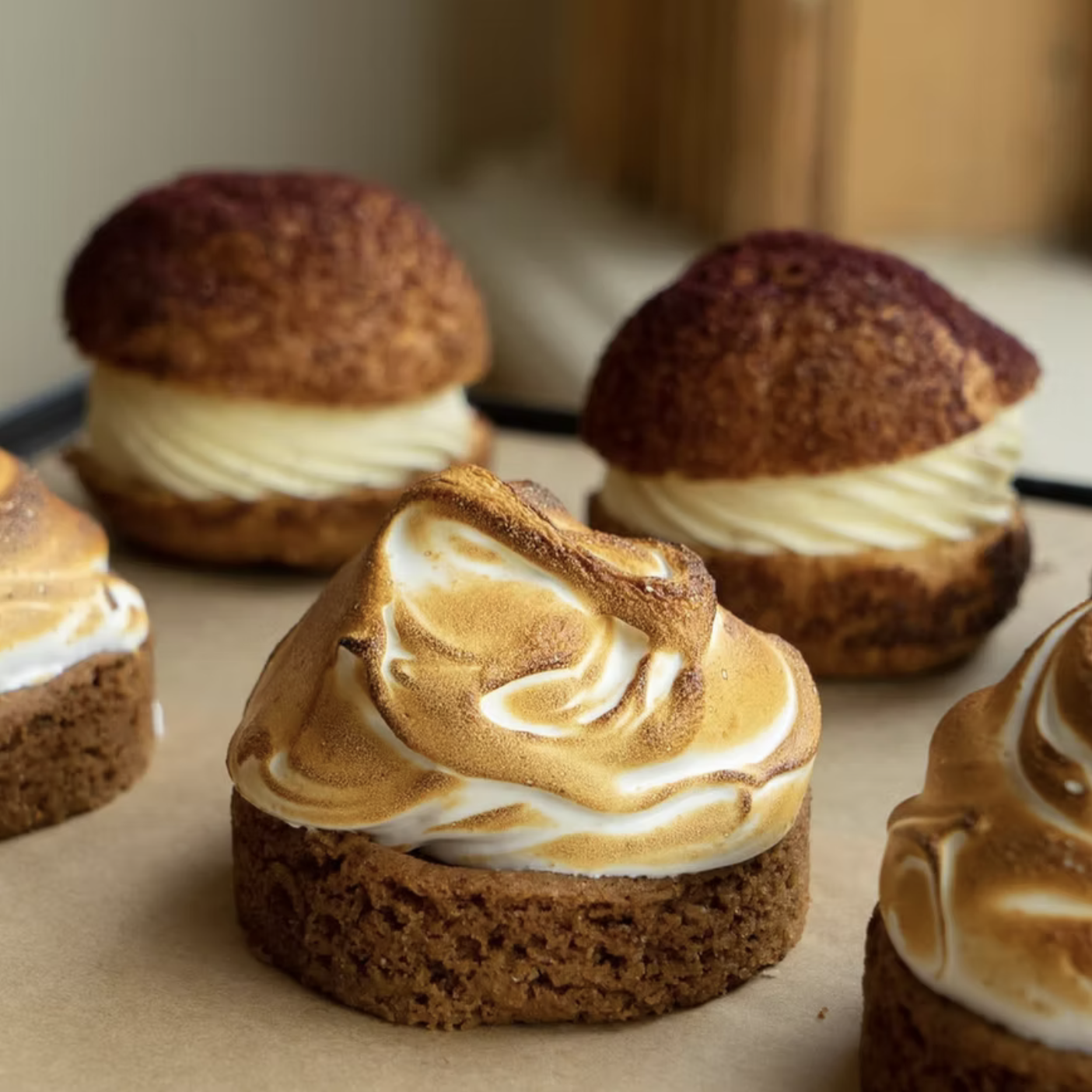 Close-up of cookies with toasted meringue and cream filling, with two more cookies in the background.