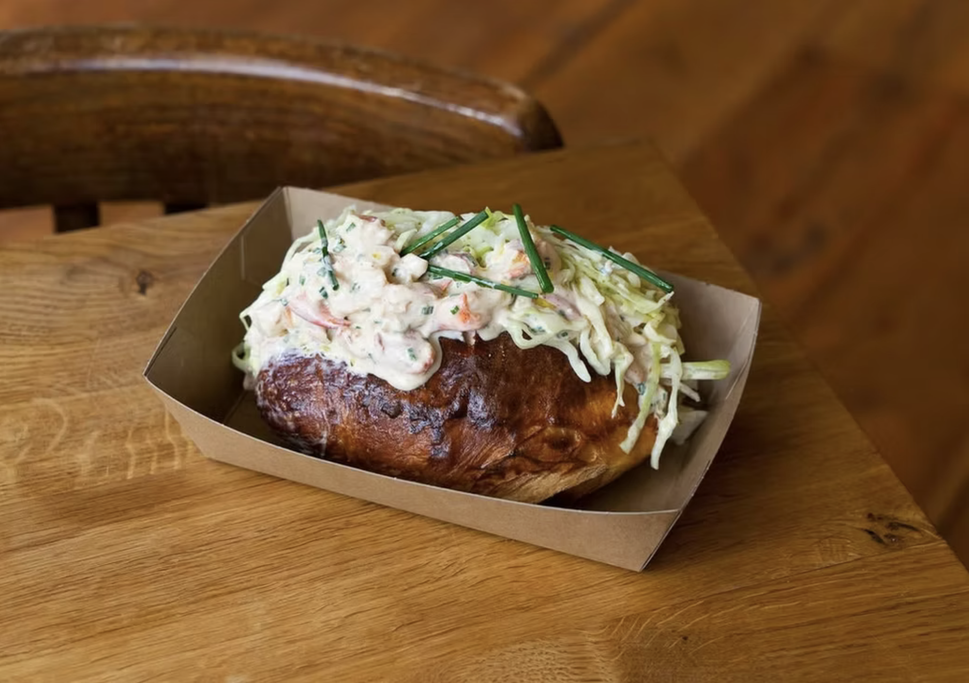 Baked pastry with a creamy salad topping in a paper food tray on a wooden table.