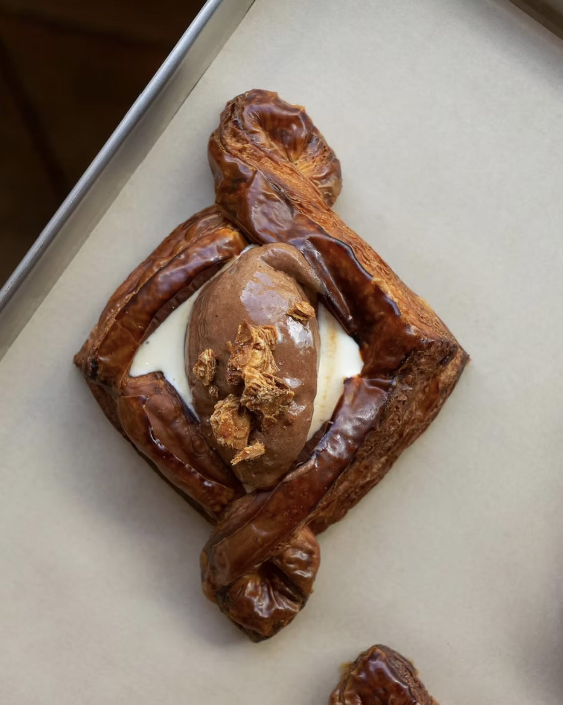 A baked pastry with a cinnamon roll shape, topped with caramelized sugar, filled with cream on a light-colored surface.