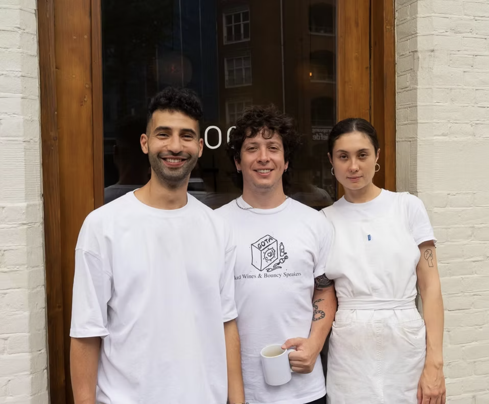 Three people standing in front of a window with a wooden frame, posed for a photo.