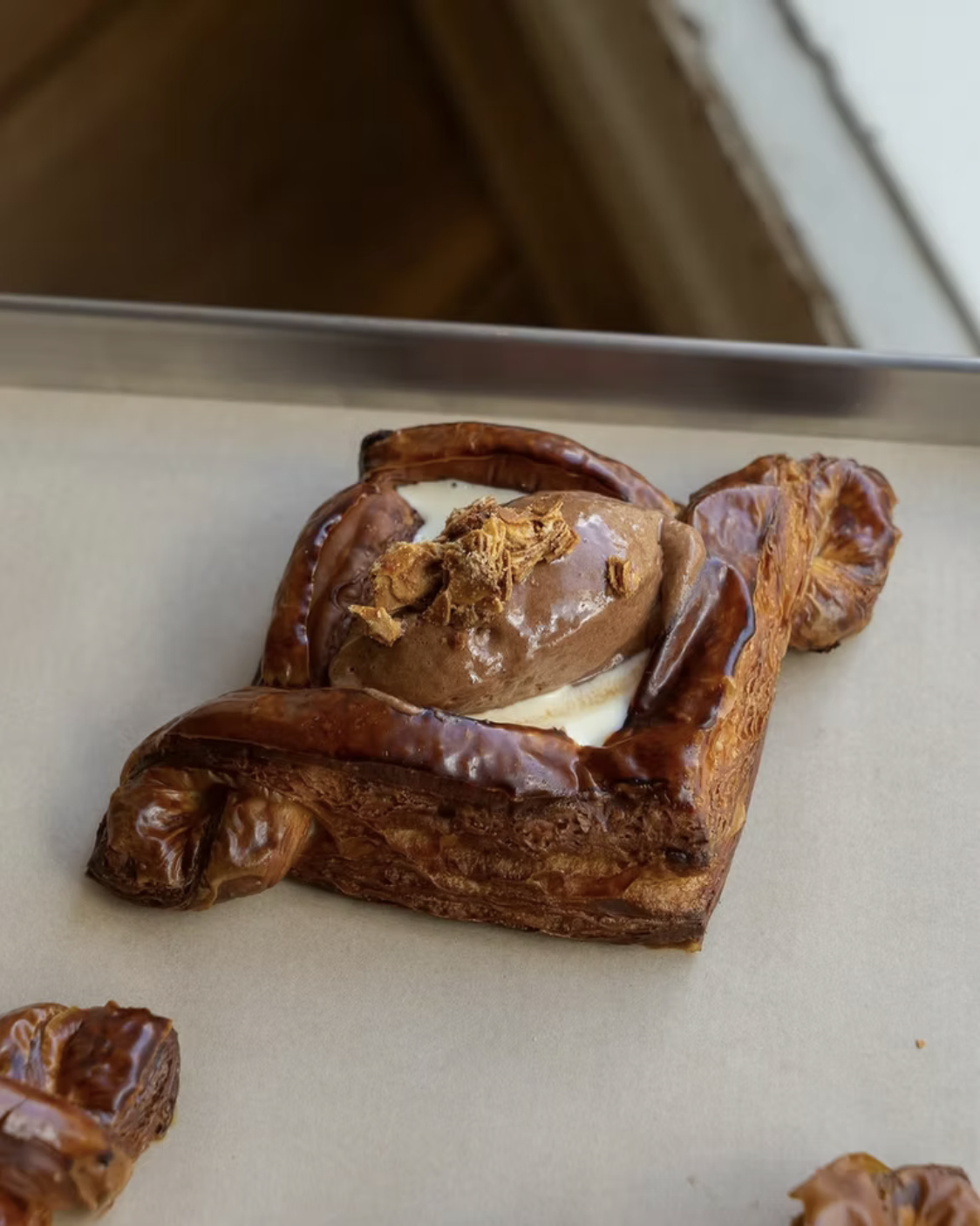 A baked pastry with a cinnamon roll shape, topped with caramelized sugar, filled with cream on a light-colored surface.