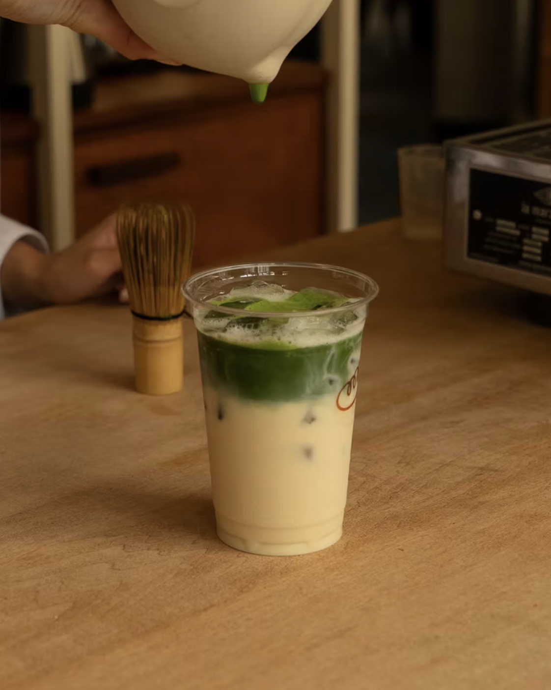 Layered beverage with matcha tea, milk, and ice, served in a plastic cup.