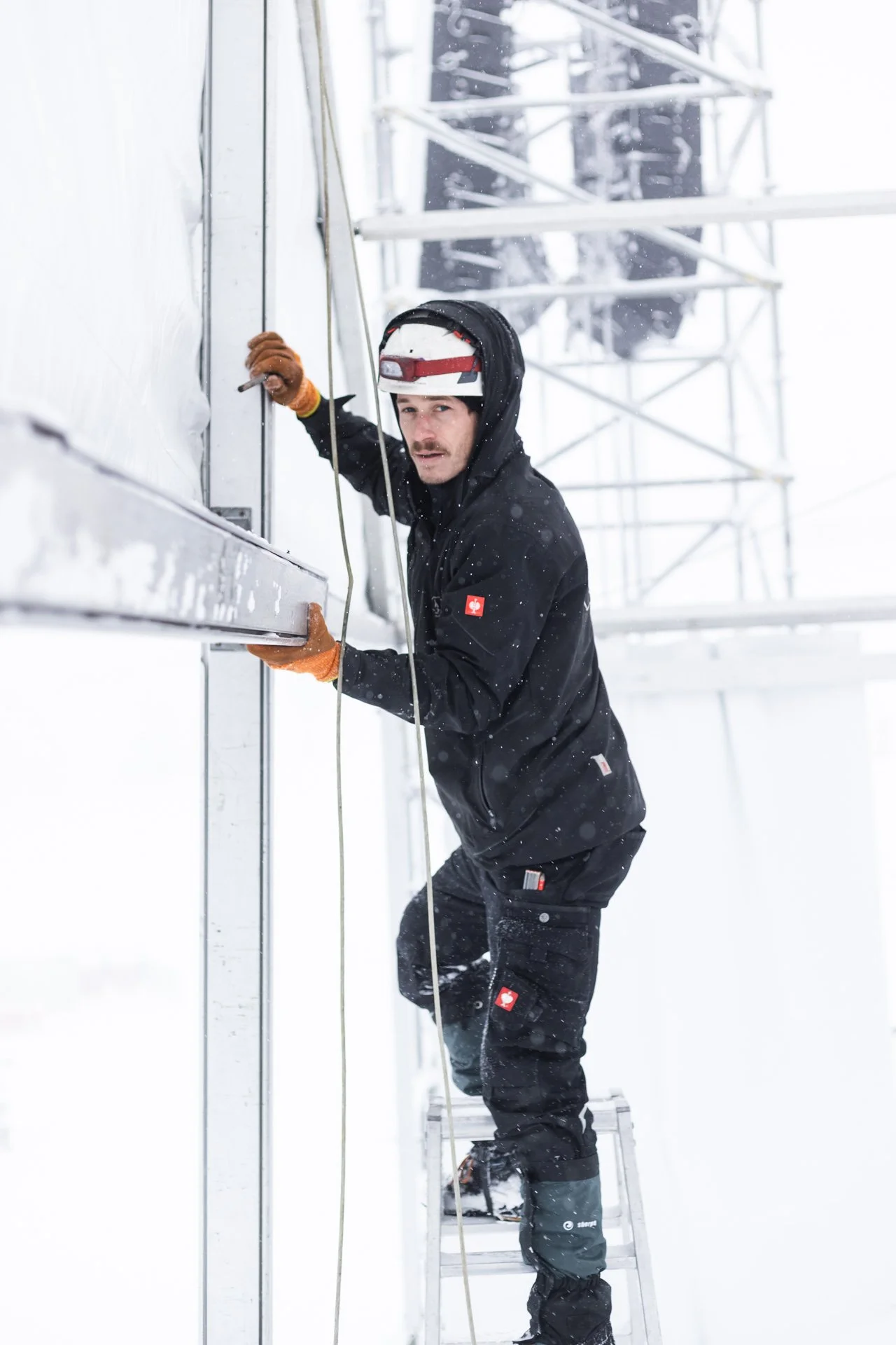 Mann auf einer Leiter arbeitet an einen Festzelt bei winterlichen Bedingungen.