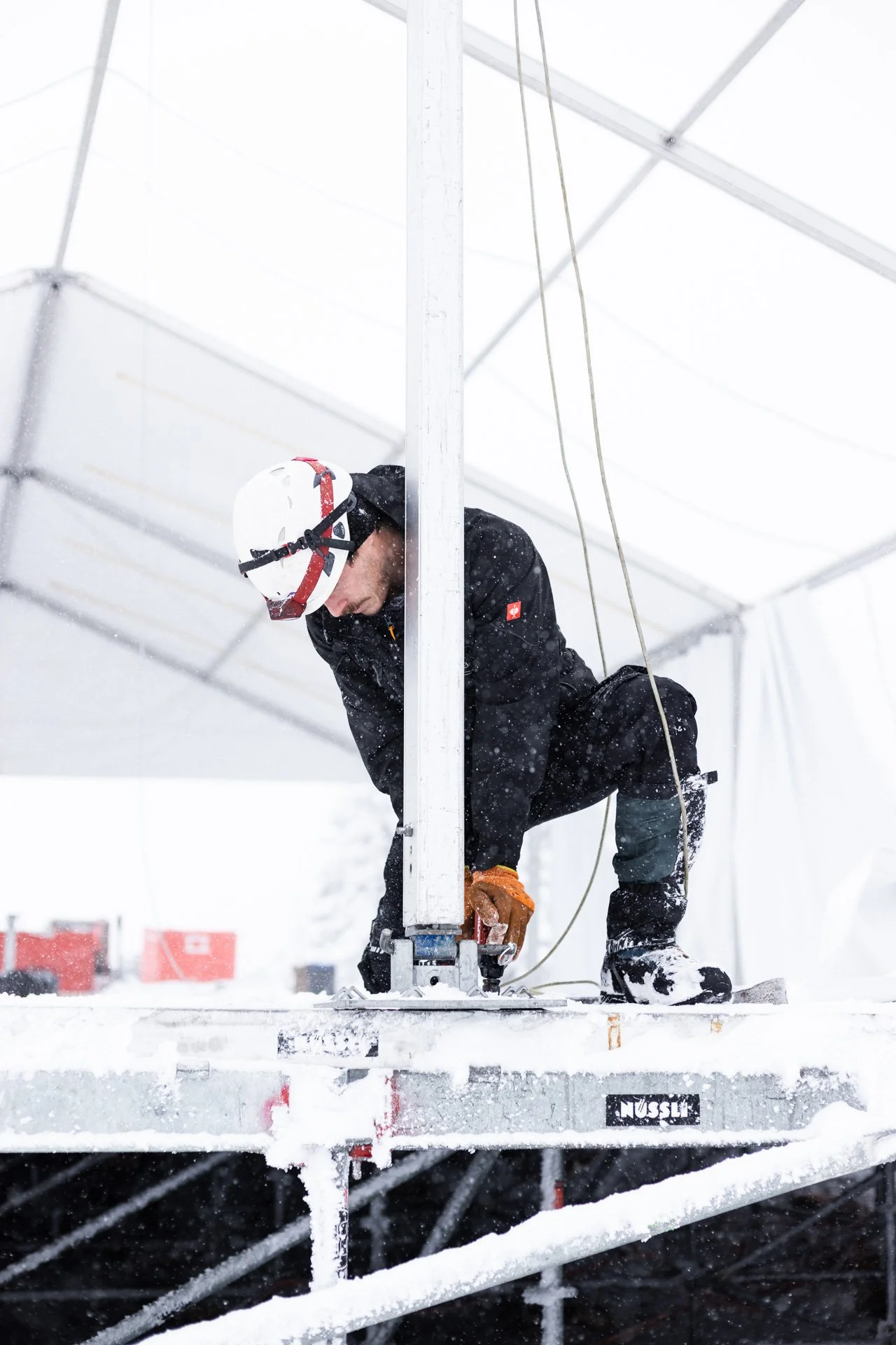 Ein Arbeiter trägt eine Kletterausrüstung und trägt eine Schutzhelm, während er an einem weißen Gerüst im Schnee arbeitet.