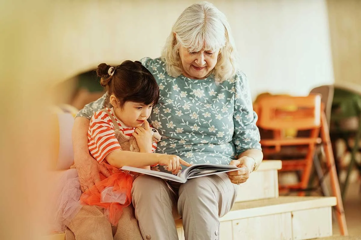 An elderly woman and a young girl sitting together, reading a book, indoors.