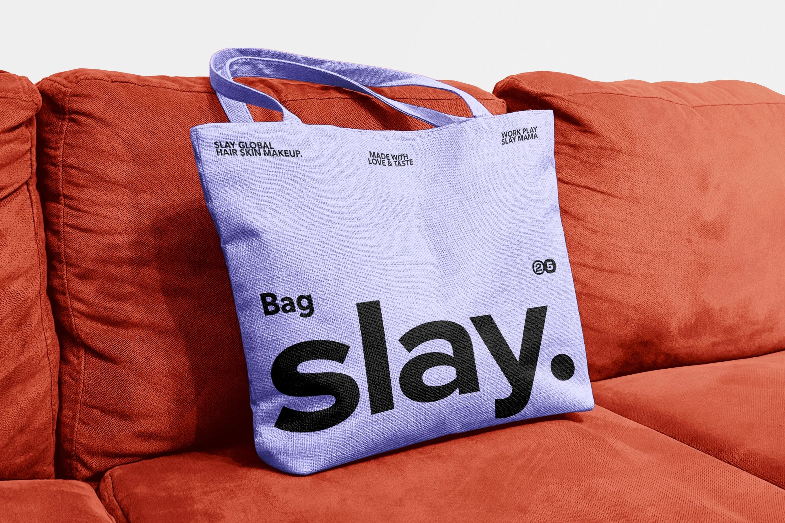 Lavender tote bag with black text that reads "Bag slay" resting on a red couch.