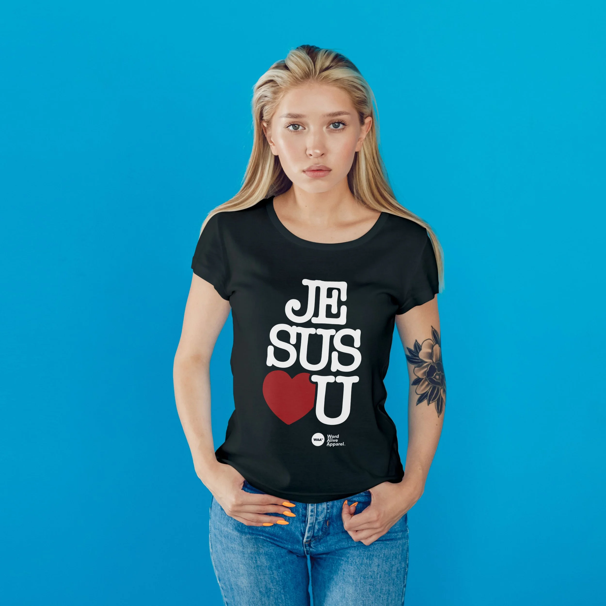 Young woman with long blonde hair wearing a black T-shirt with the words 'JE SUS U' and a red heart, standing against a blue background.