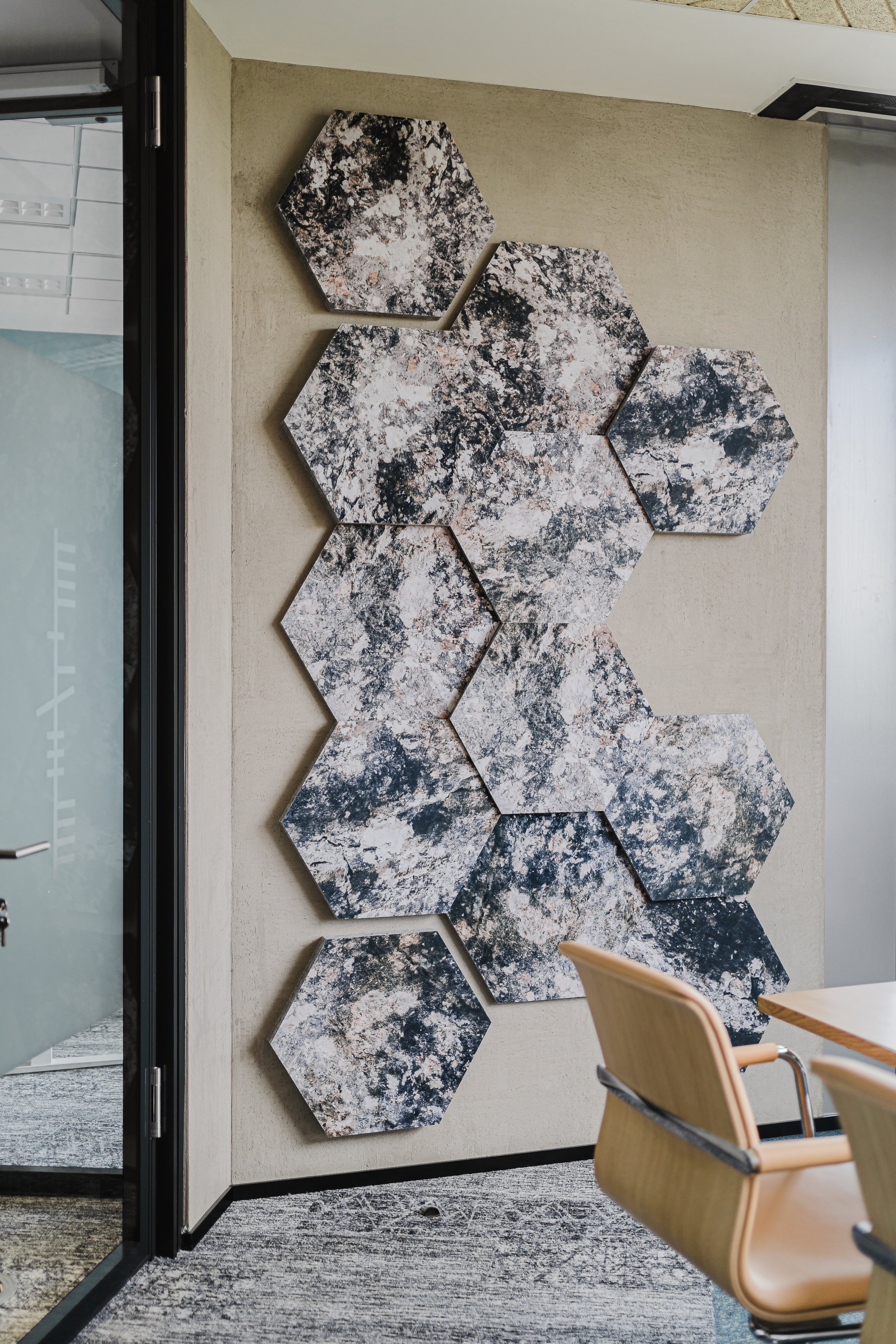Decorative wall art consisting of eight hexagonal panels with a marbled black, white, and brown pattern located on a beige wall in an office or conference room.