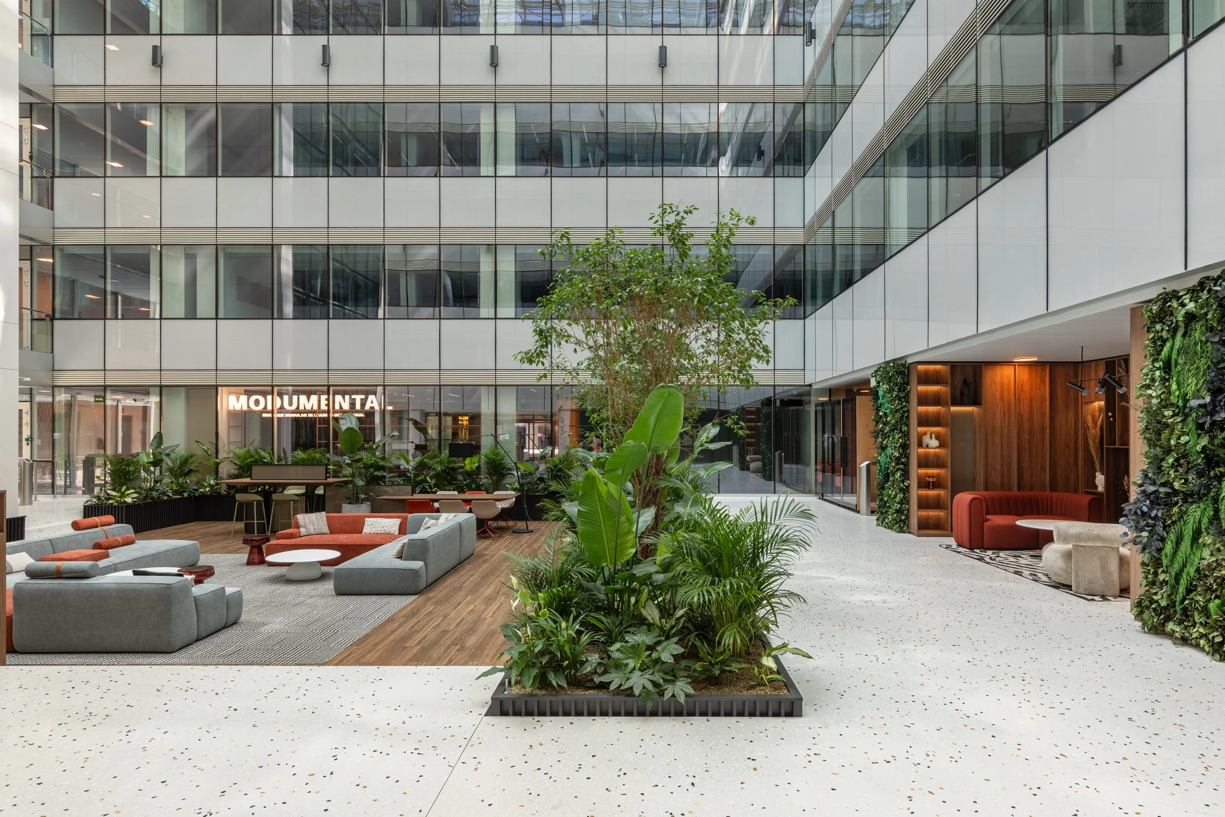 Modern office lobby with seating area, indoor plants, and glass exterior walls.