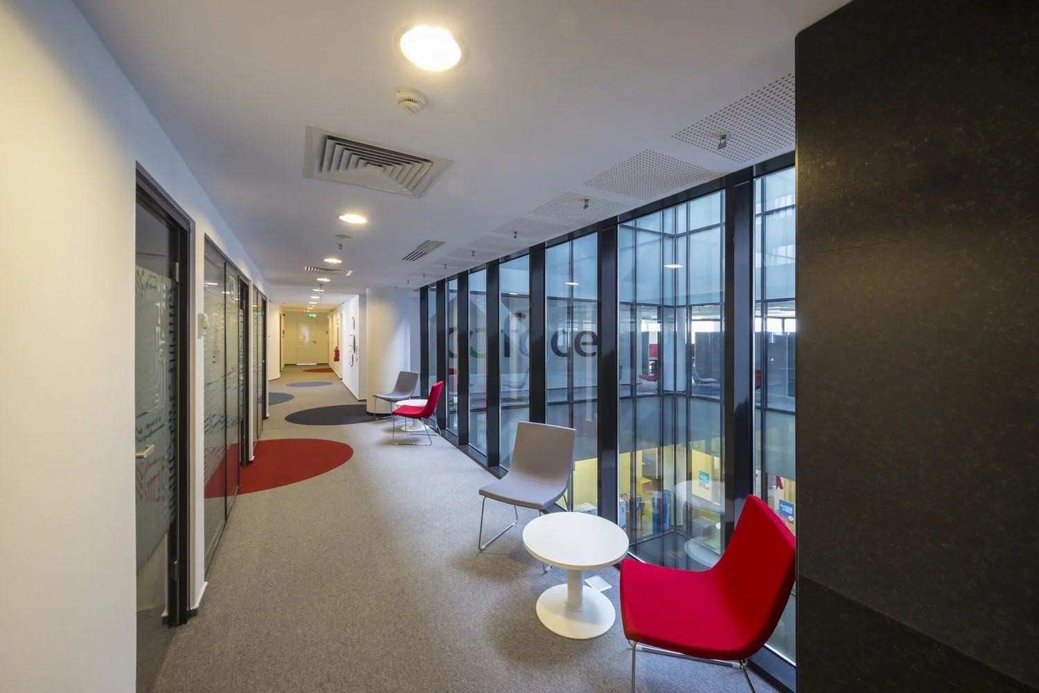 Modern office corridor with colorful chairs and large windows.