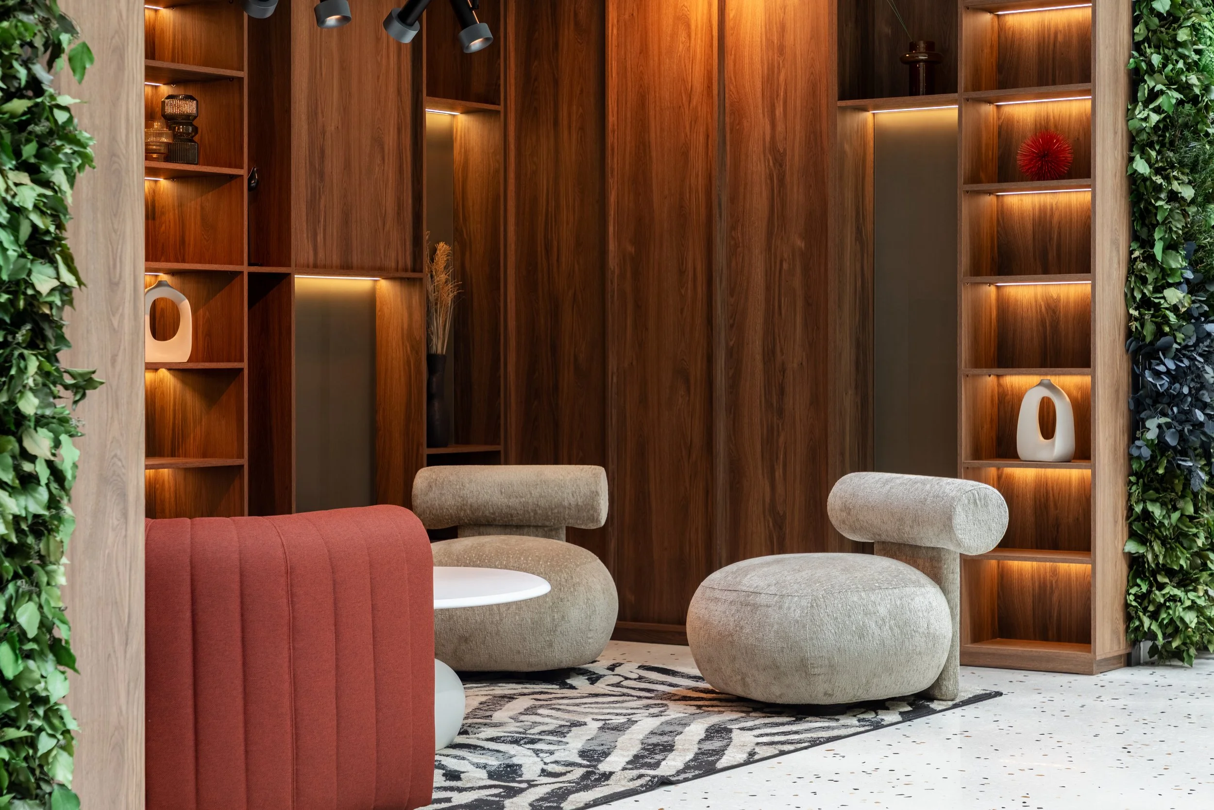 Modern interior living space with wooden shelving, beige chairs, a patterned rug, and decorative items.