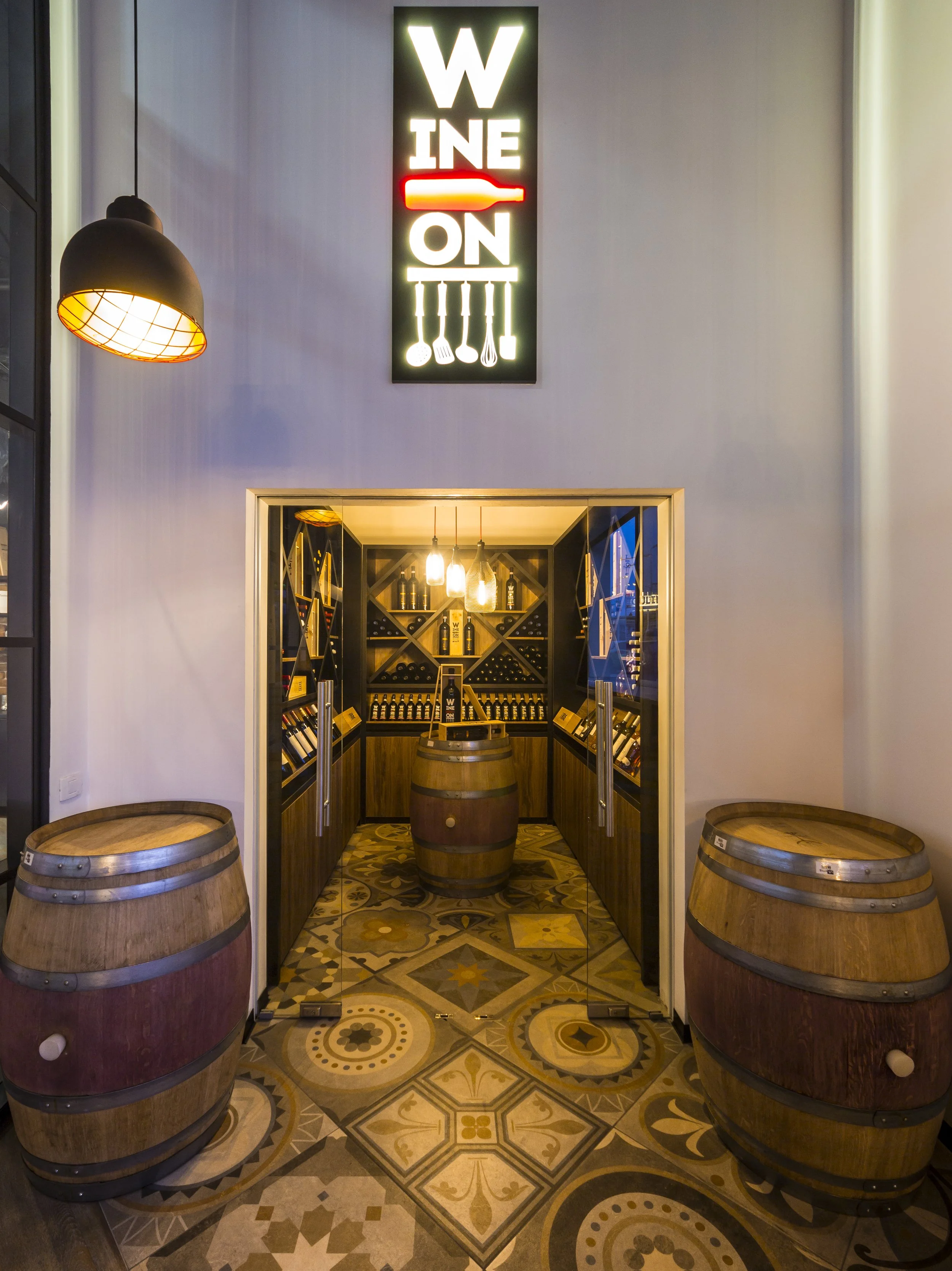 Interior view of a wine shop entrance with a sign above and two wine barrels on either side of the door, patterned tile floor.