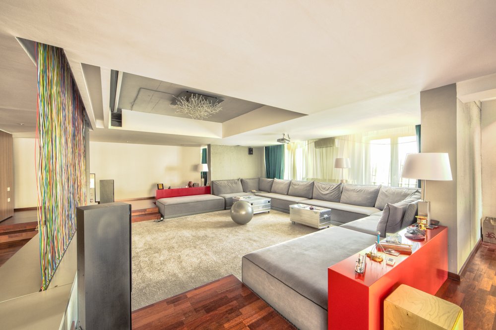 Bright living room with large gray sectional sofa, a red accent wall, a silver exercise ball, and colorful curtains.