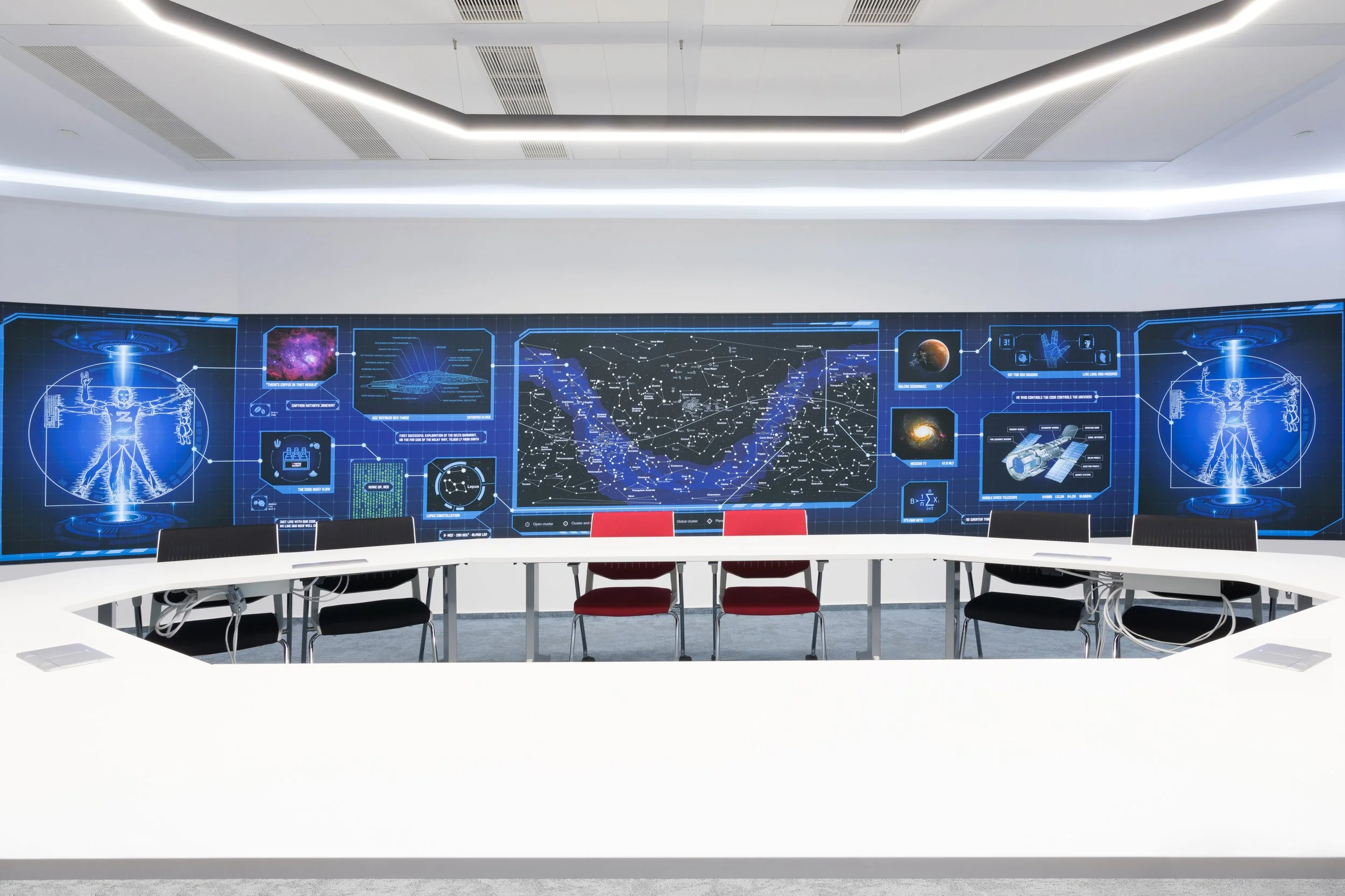 A circular conference table in a high-tech room with a large digital display wall showing futuristic space and technology diagrams.
