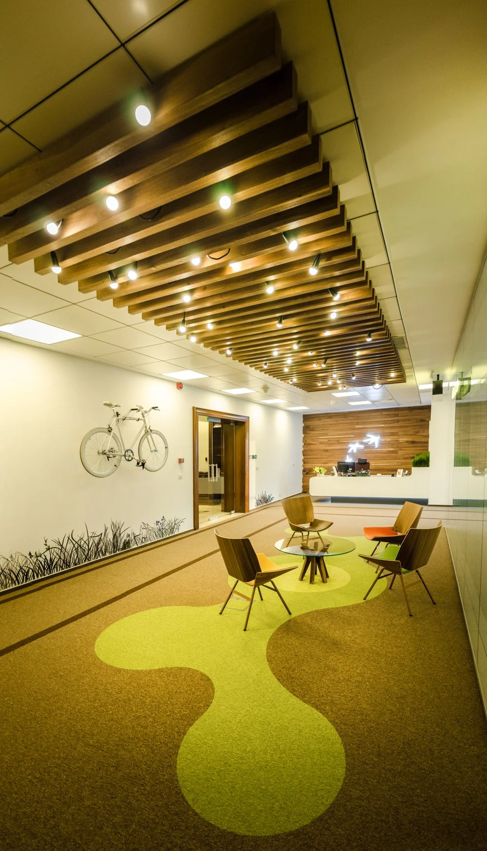 Modern office waiting area with colorful carpet, wooden chairs, and a reception desk in the background.
