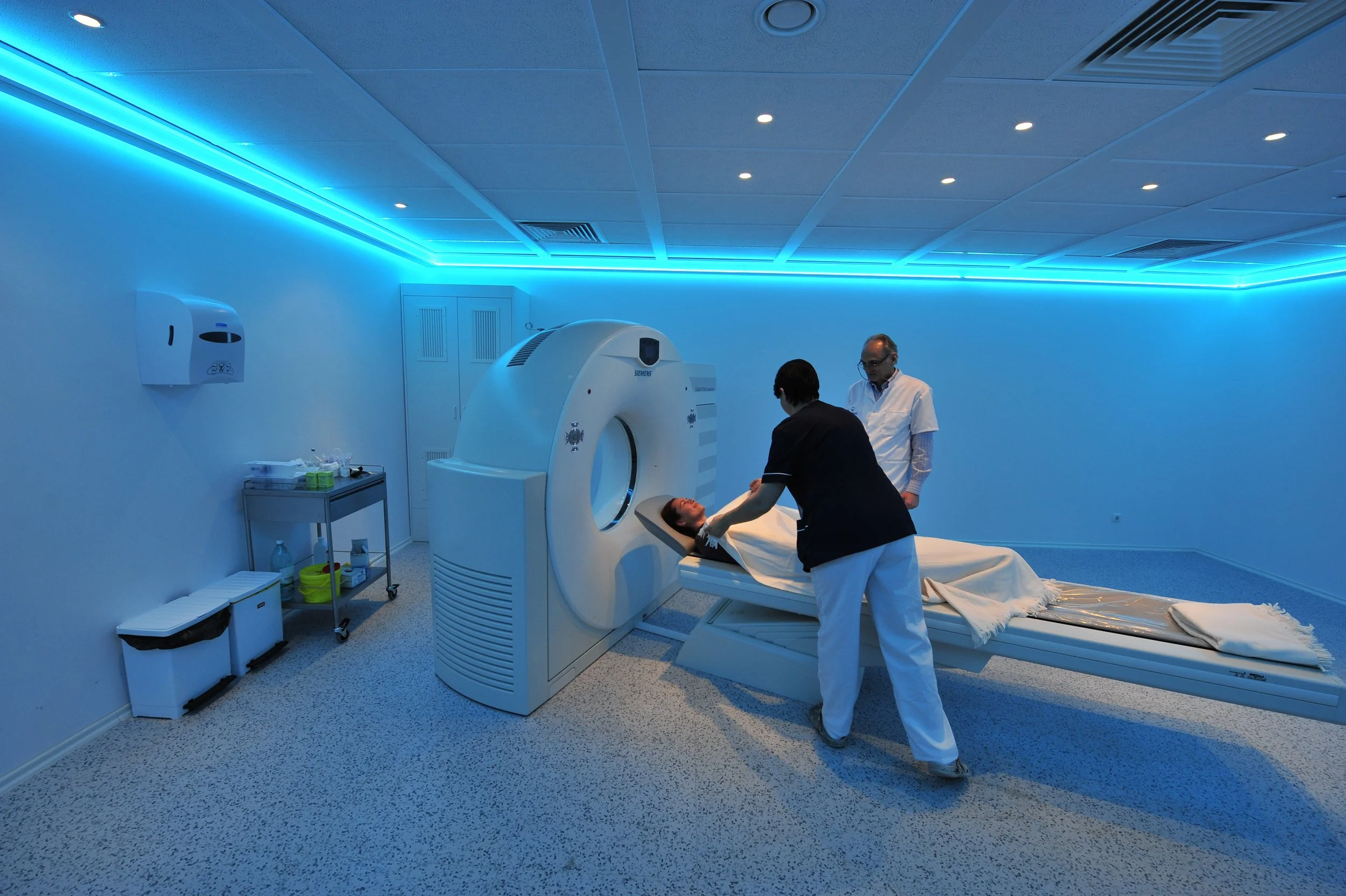 Hospital room with a woman lying on a bed being positioned into an MRI machine, with two medical professionals assisting.