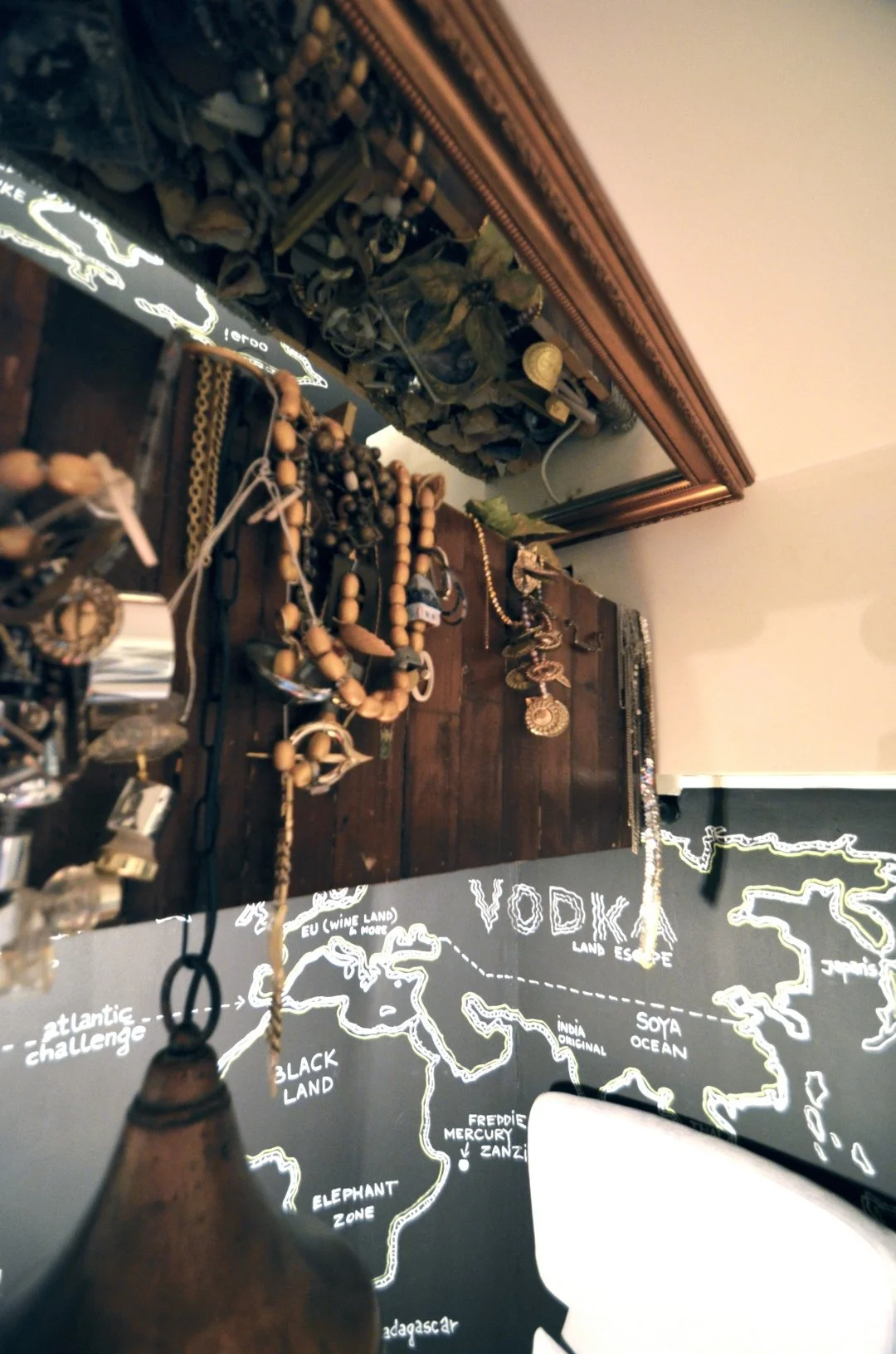 A collection of jewelry, including necklaces, and a blackboard map of the world with place names written in white, including 'Vodka' and various countries.