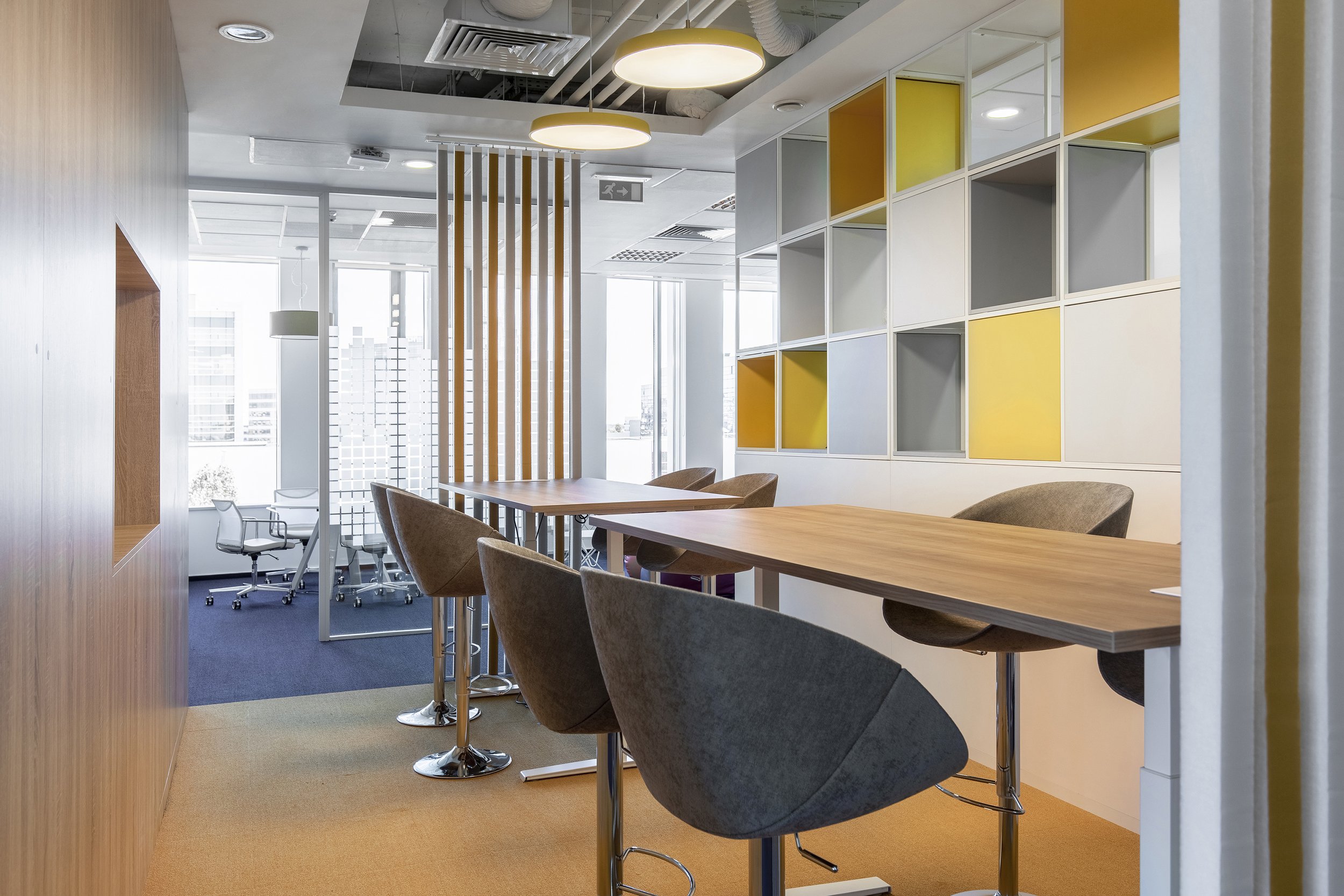 Modern office space with high tables, comfortable chairs, wooden flooring, and colorful shelving units.