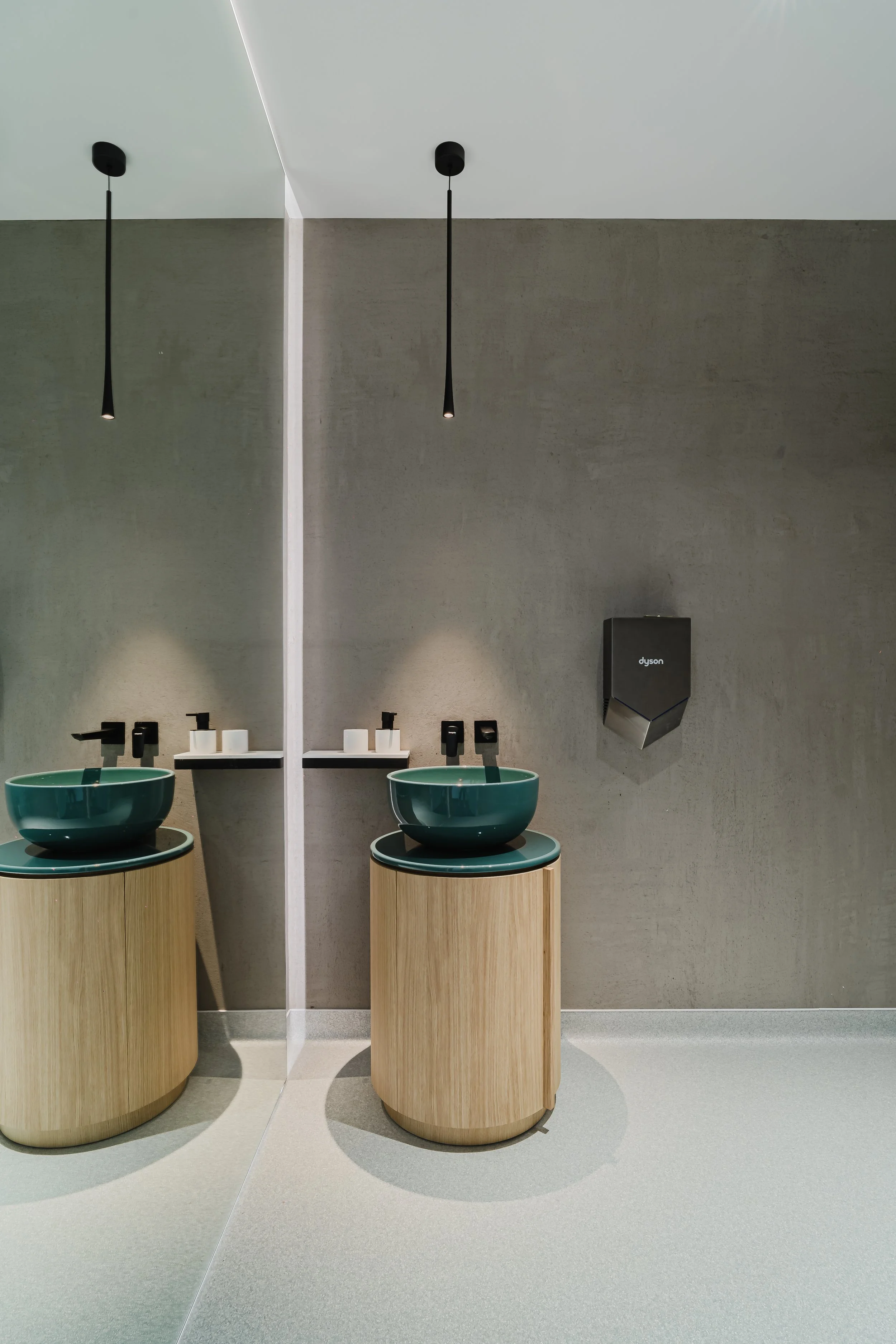 Modern bathroom with two green vessel sinks on round wooden cabinets, black faucets, a mirror reflecting the sinks and black pendant lights.