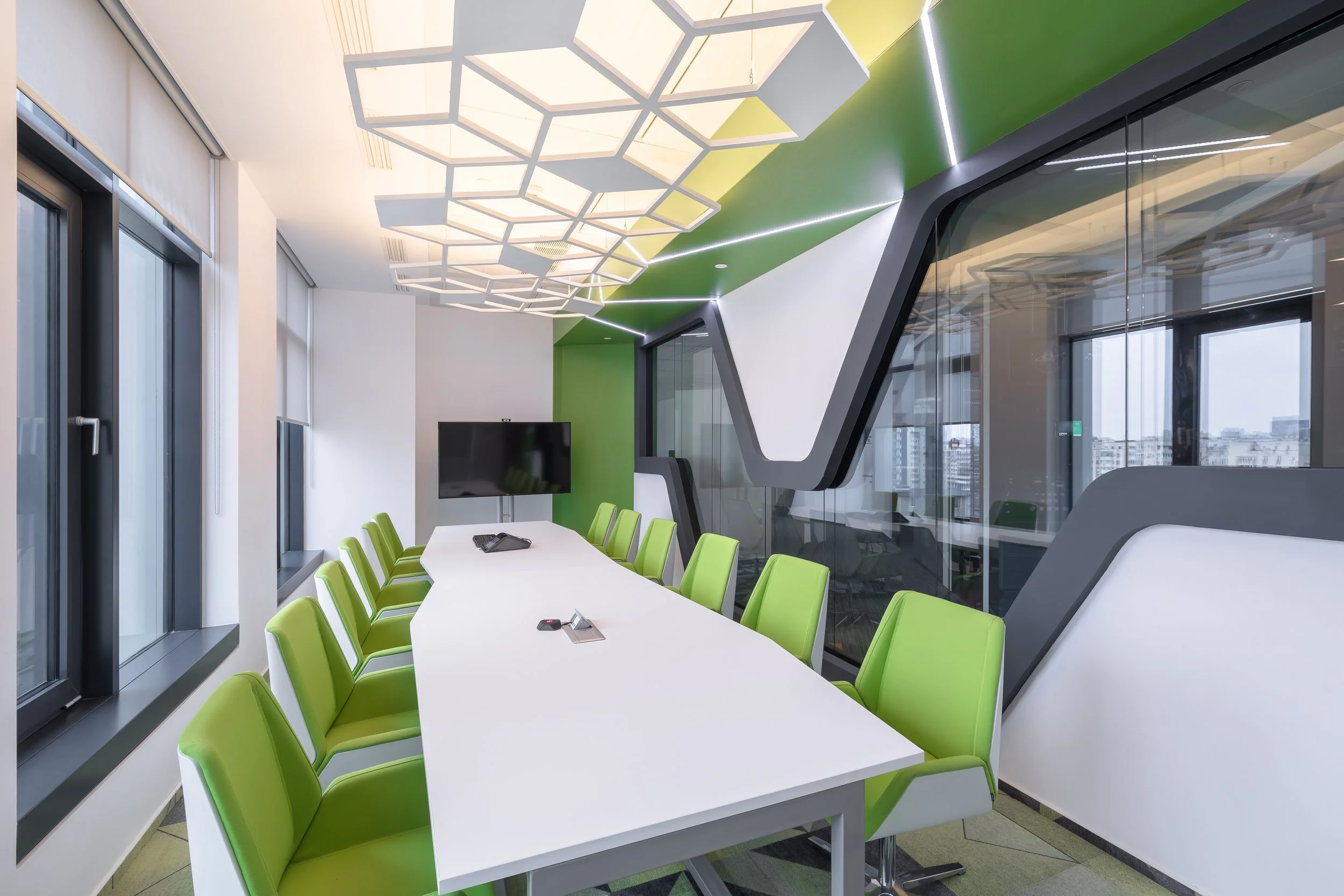 Modern conference room with a long white table, lime green chairs, a large flat-screen TV, and decorative ceiling lighting.