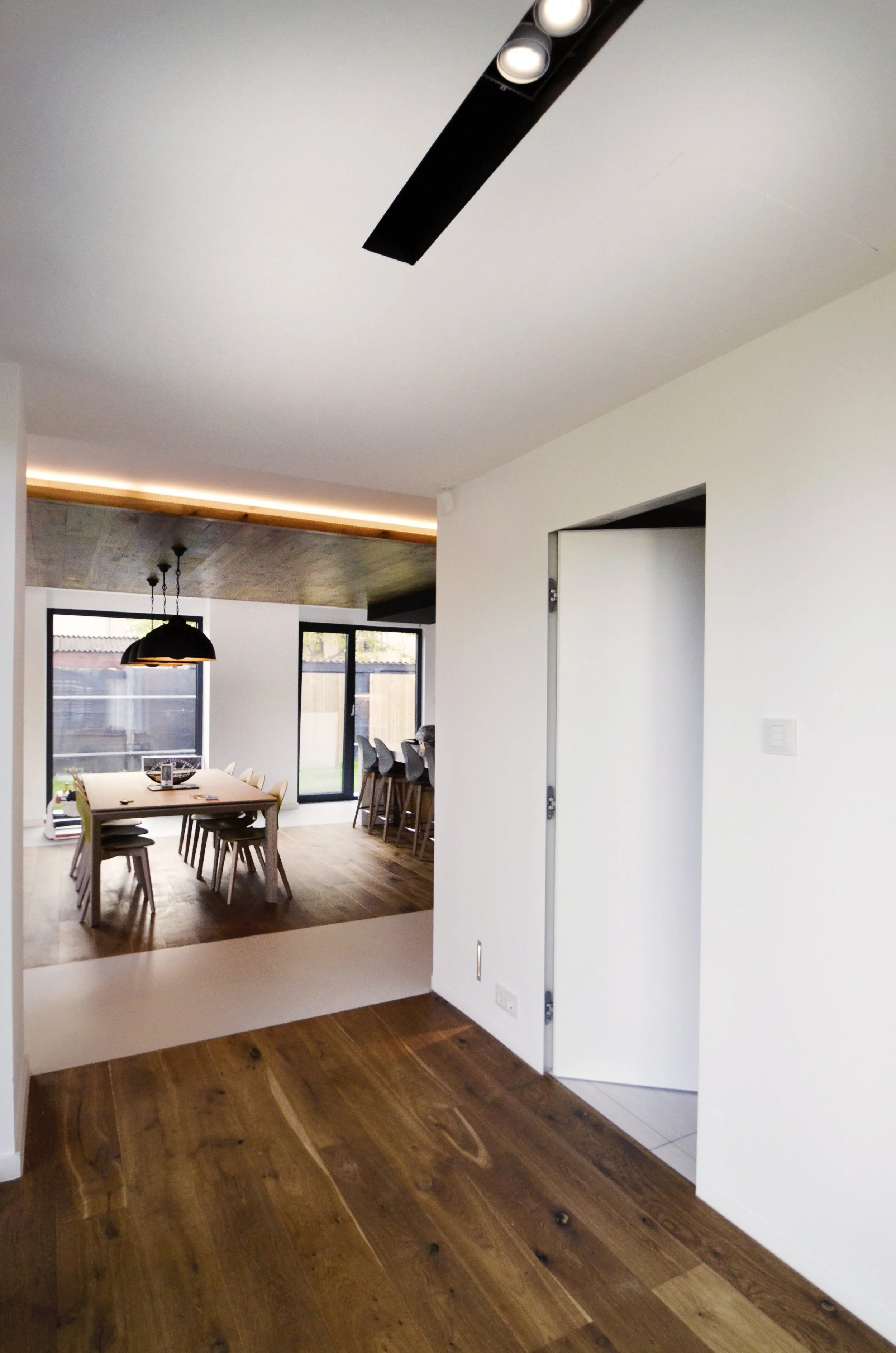 Interior of a modern open-concept dining and kitchen area with wooden floors, a dining table, chairs, and sliding glass doors.