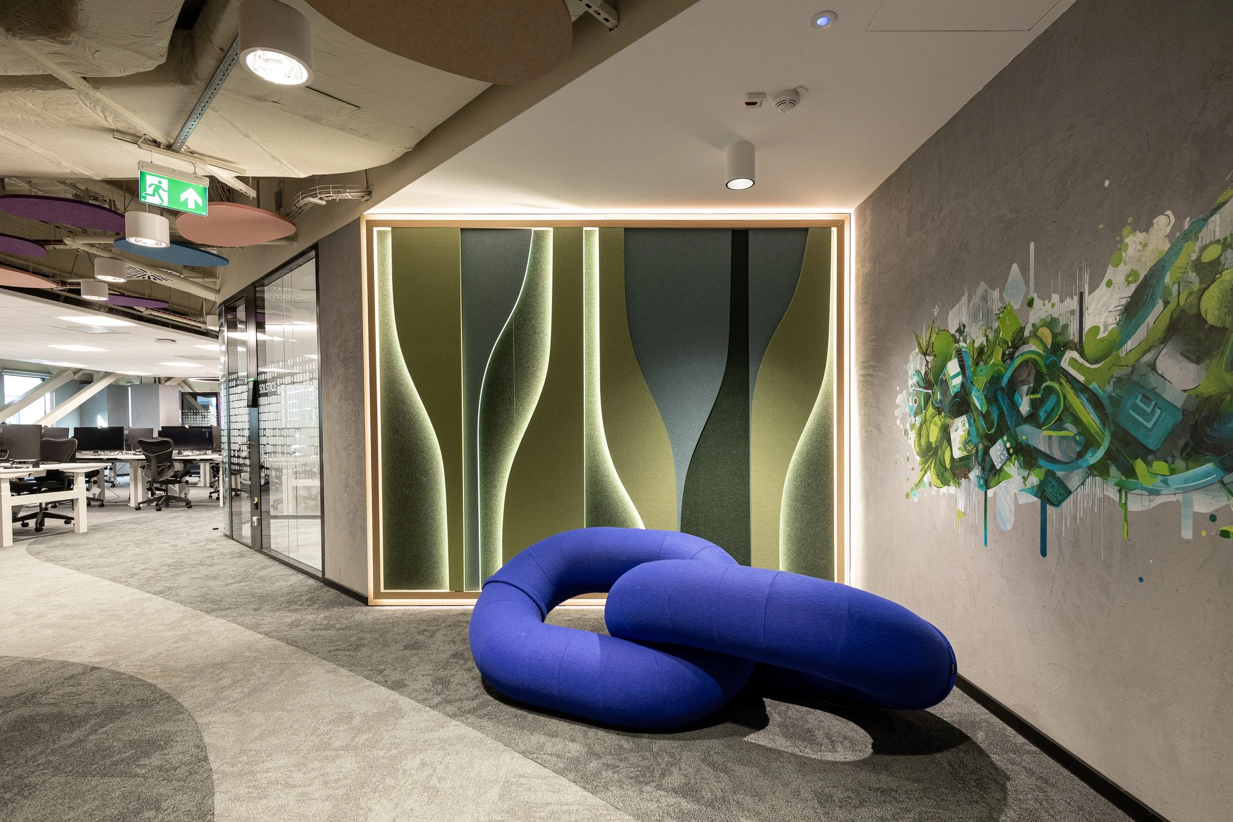 Modern office interior with patterned wall, colorful abstract wall art, and a blue, curved lounge chair.