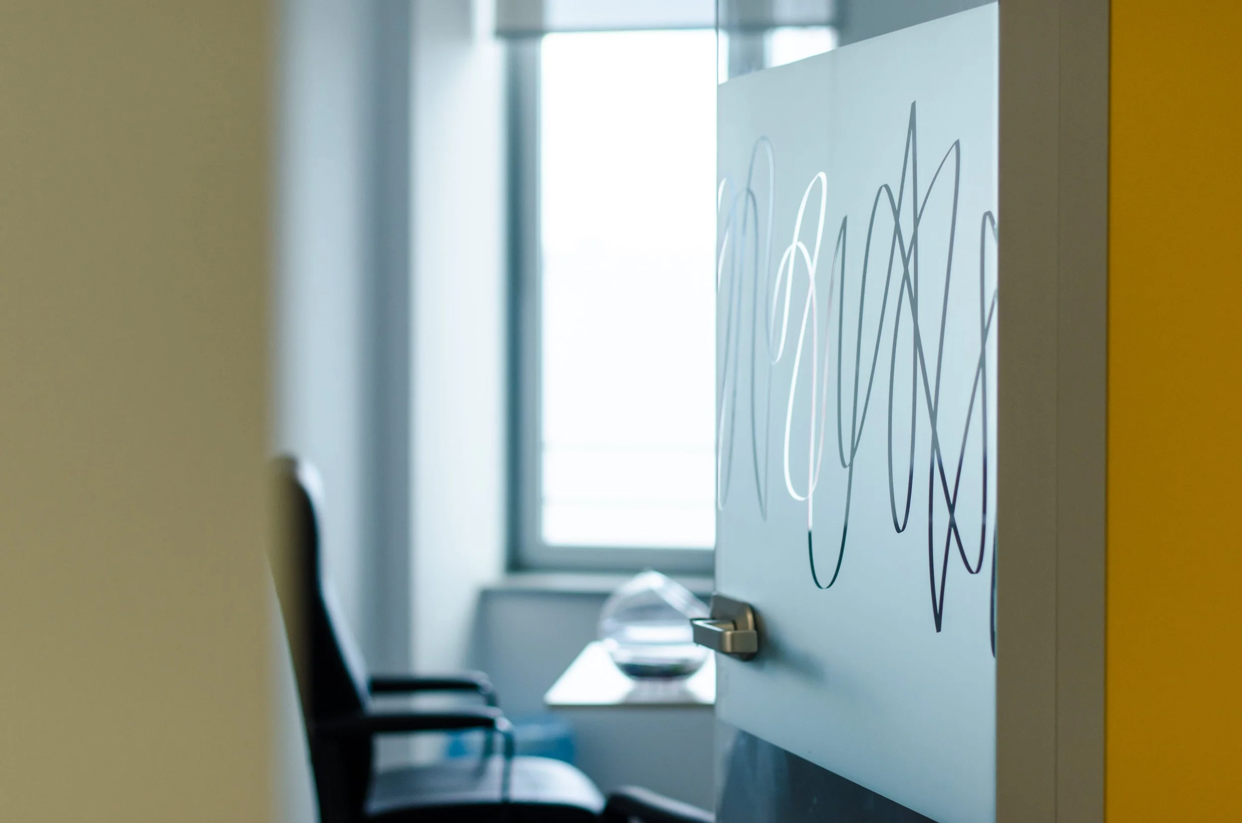 View of a whiteboard with colorful scribbles, and chairs in a conference room with a window in the background.