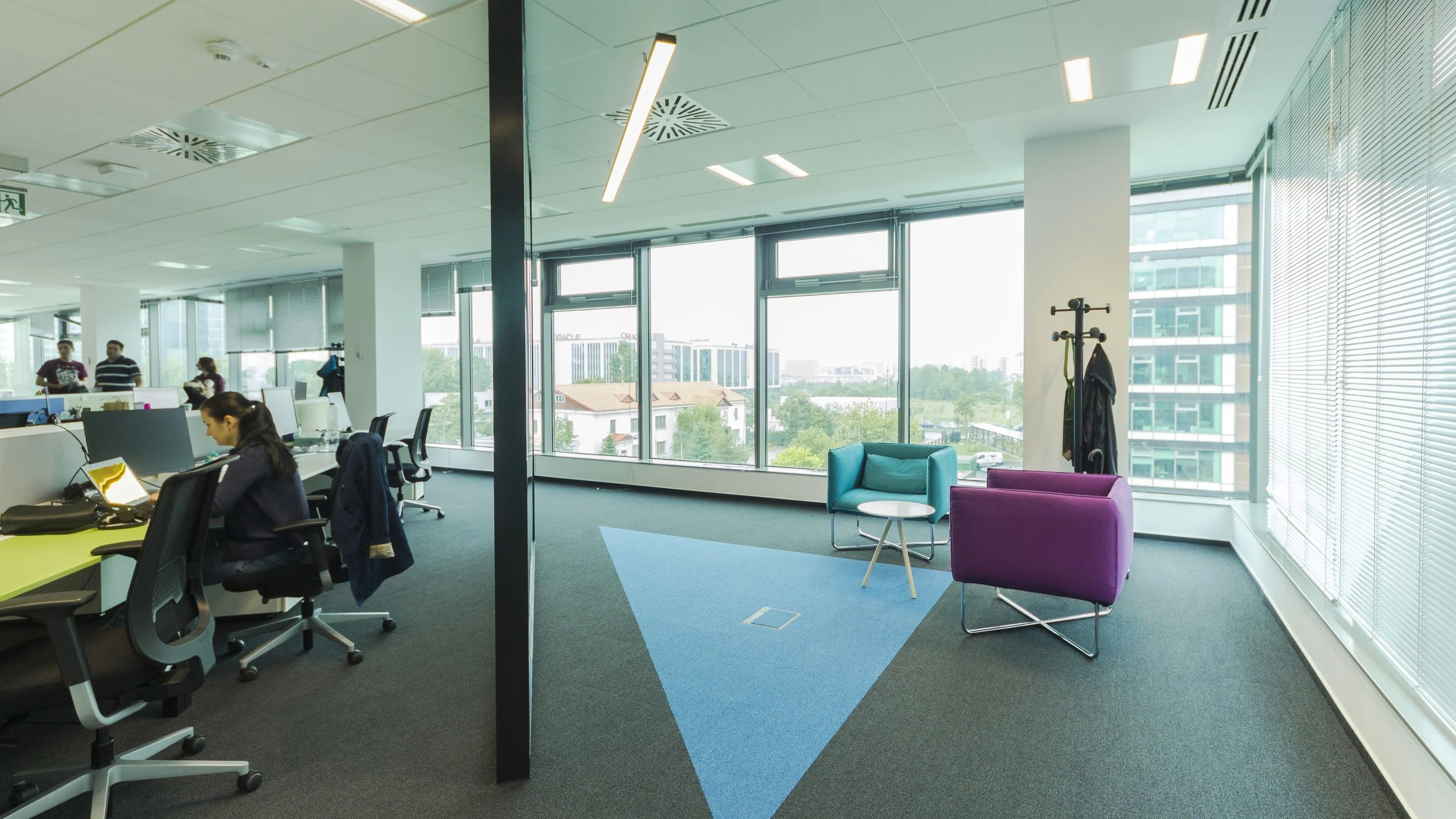 Modern office space with large windows, two colorful chairs, a small round table, and a coat rack.