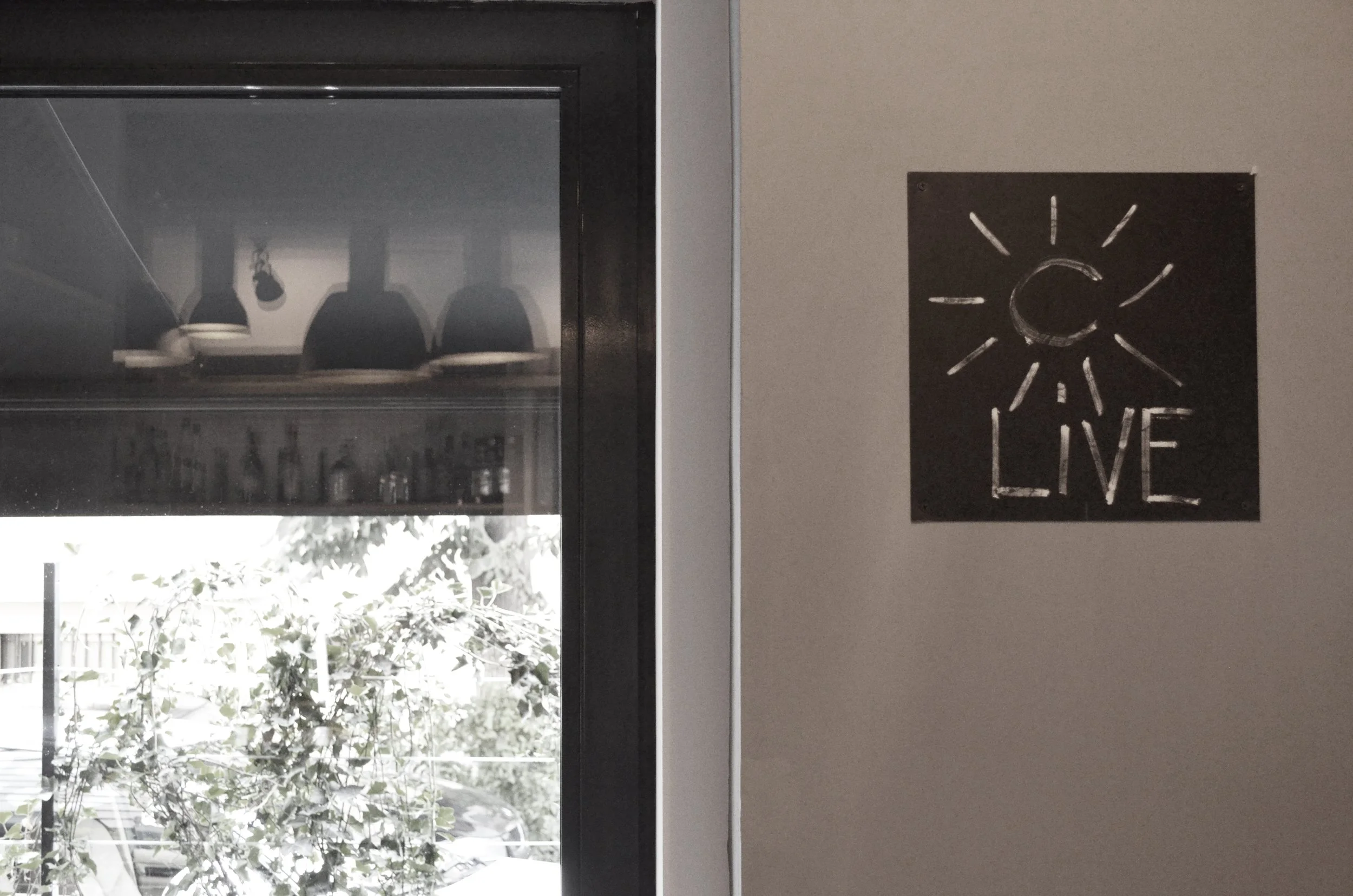 A wall with a black sign featuring a sun drawing and the word 'LIVE' written underneath.