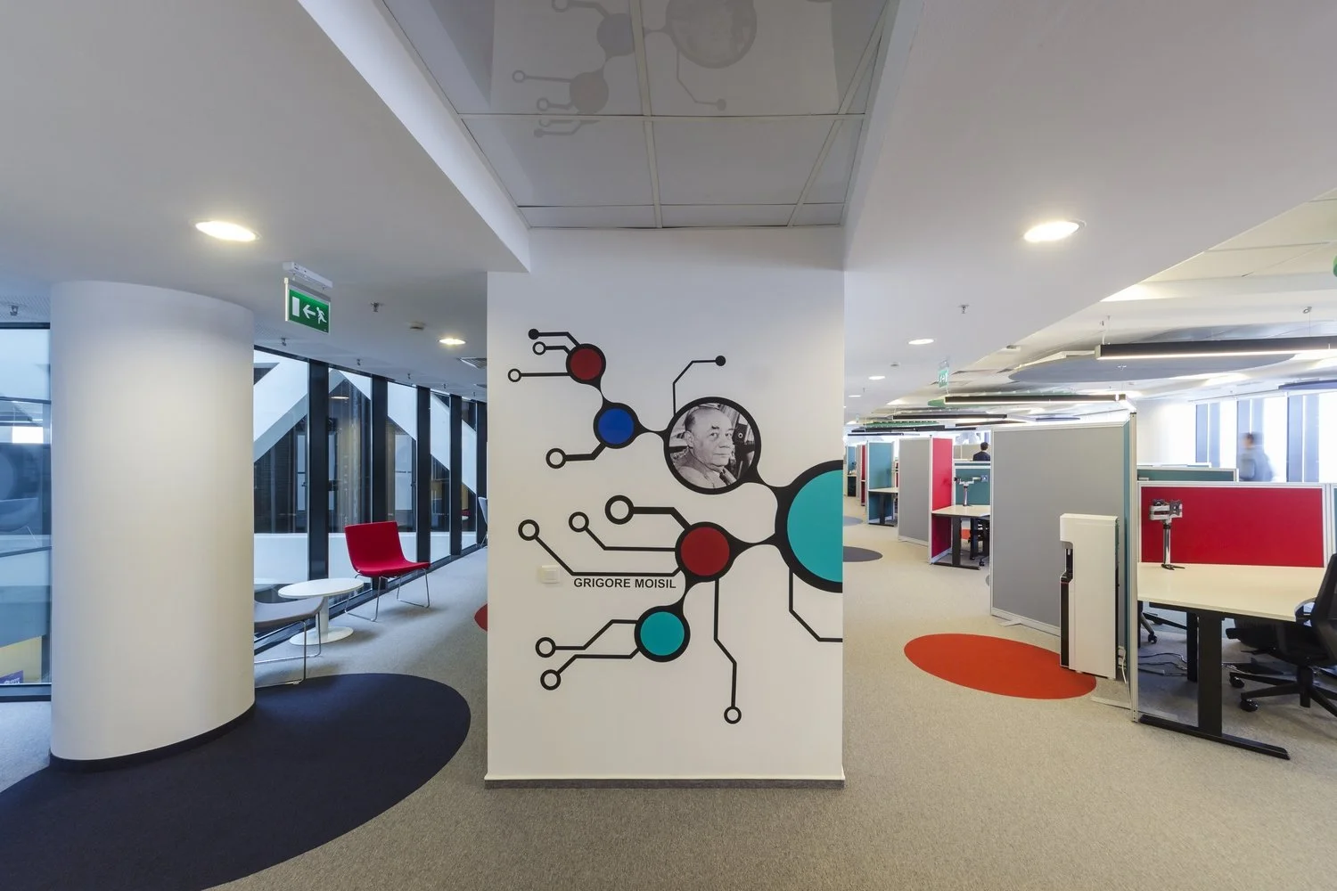 Modern office space with colorful furniture and graphic wall art featuring a photo of an elderly man and abstract design elements.