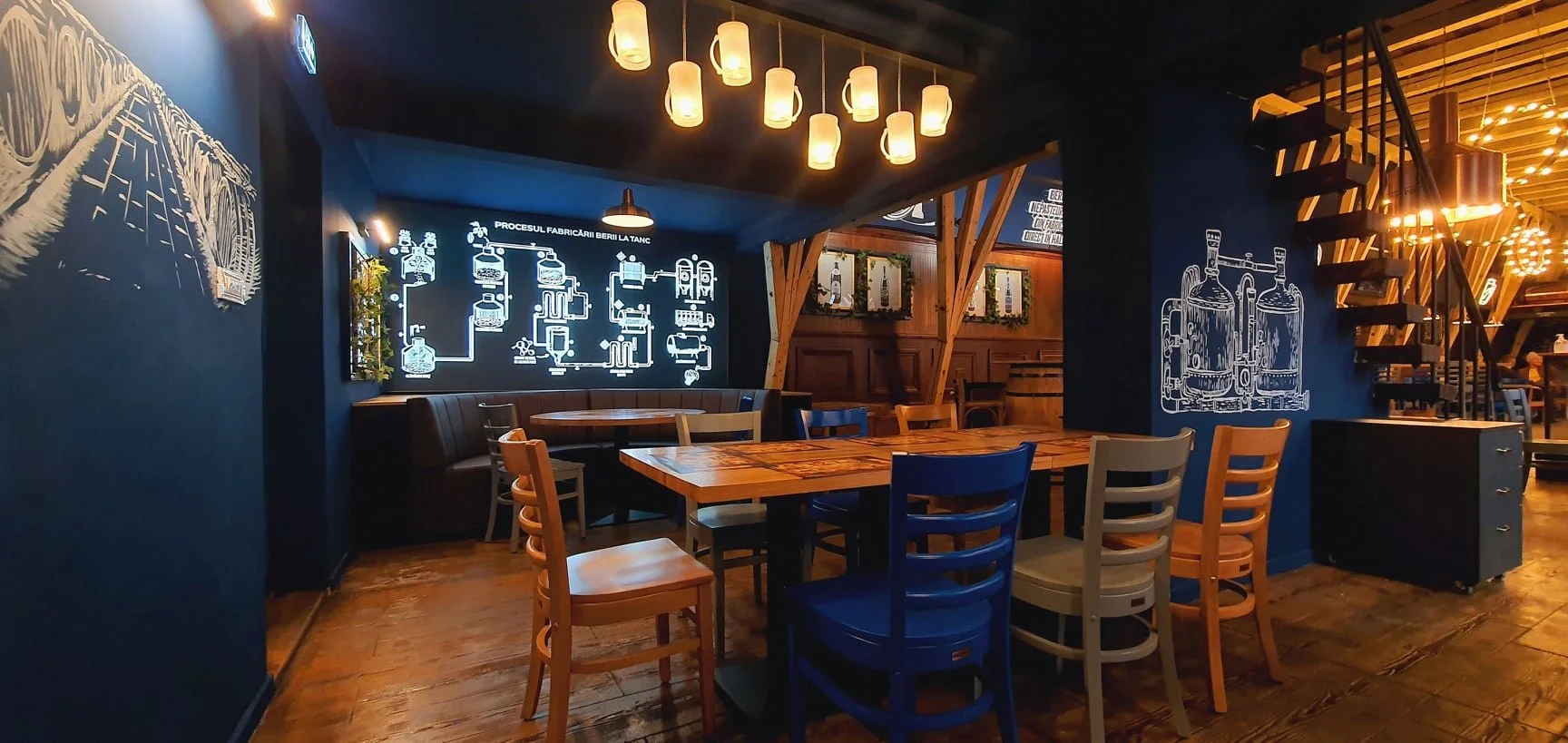 Interior of a rustic restaurant with wooden furniture, blue walls decorated with diagrams and sketches, and hanging pendant lights.