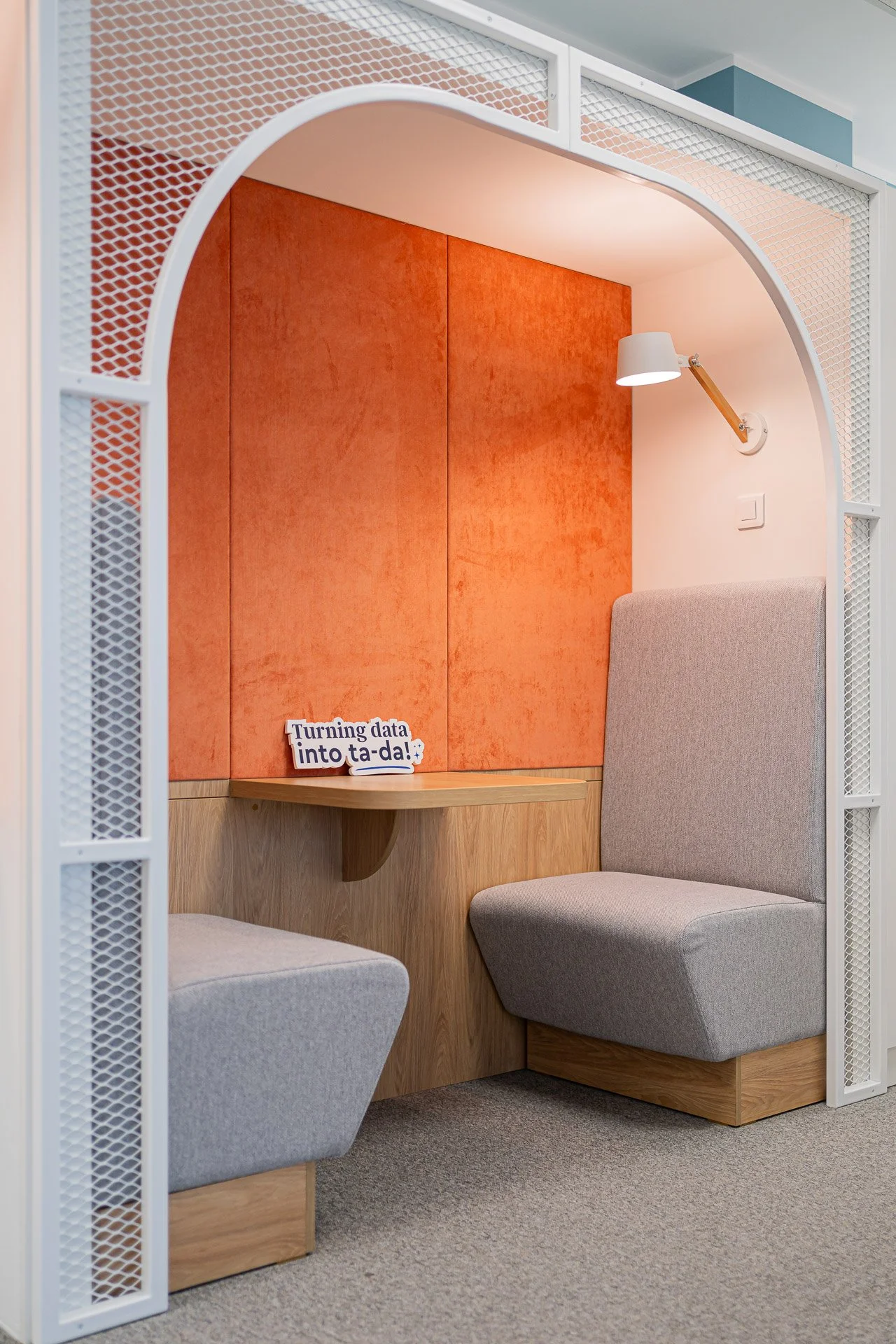 A cozy office pod with cushioned seating, pink walls, a wall-mounted lamp, and a small sign that reads 'Turning data into ta-da!'