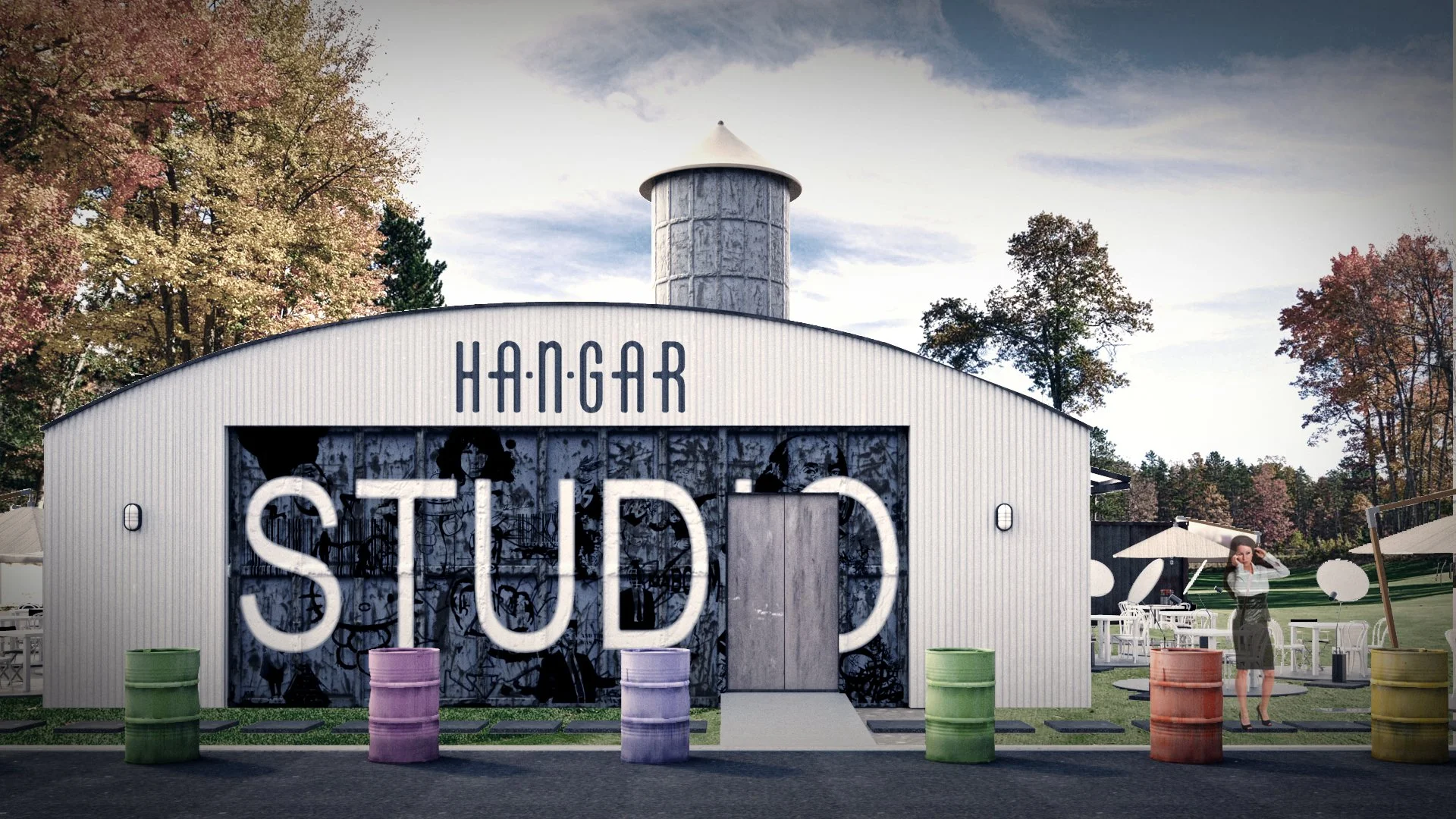 A modern building with corrugated metal siding labeled 'HANGAR STUD' with a large mural and graffiti in front, colorful barrels in the foreground, and a woman standing outside on a patio with umbrellas and chairs during daytime.