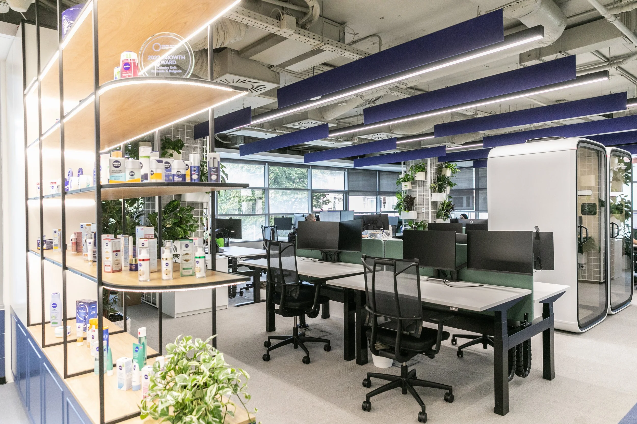 Modern open-concept office with workstations, large windows, and interior plants.