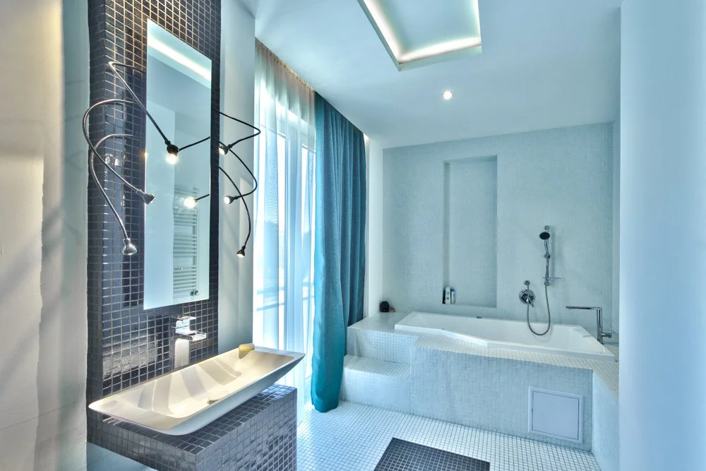 Modern bathroom with a bathtub, a sink with a mirror, blue curtains, and mosaic tiles.