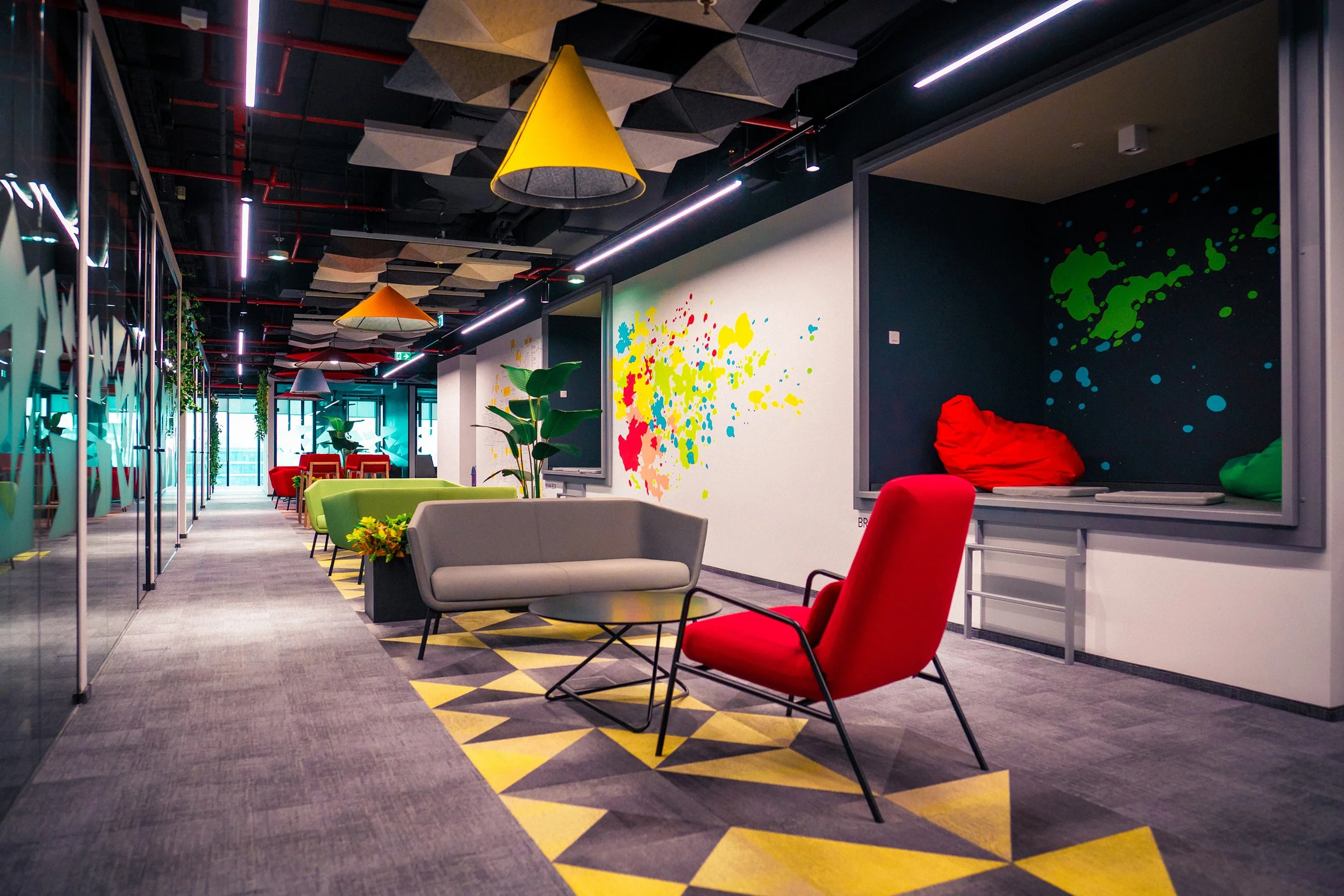 Modern office lounge area with colorful chairs, bean bags, and abstract wall art