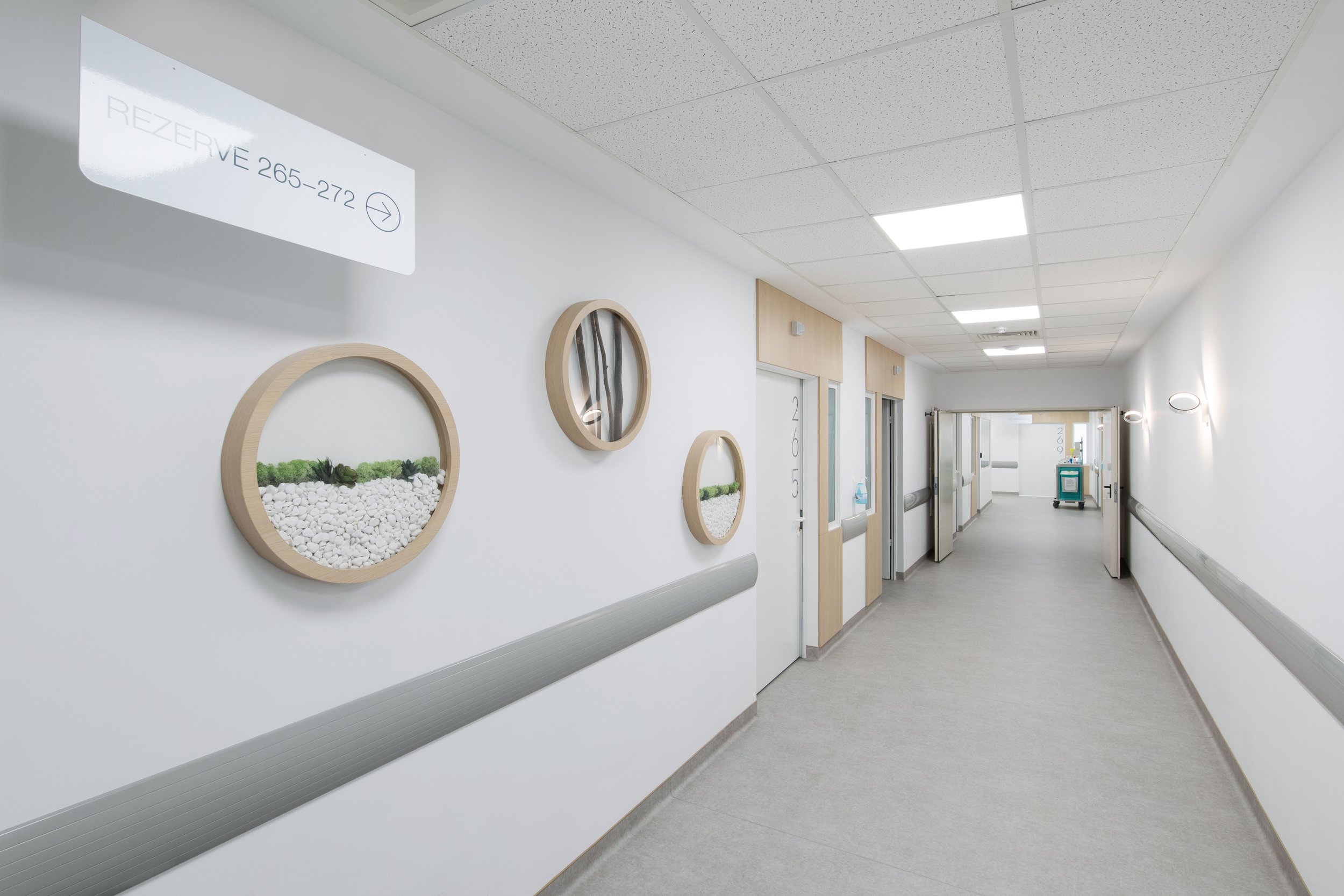 Empty hospital corridor with framed wall art and a sign directing to reserve 265-272.