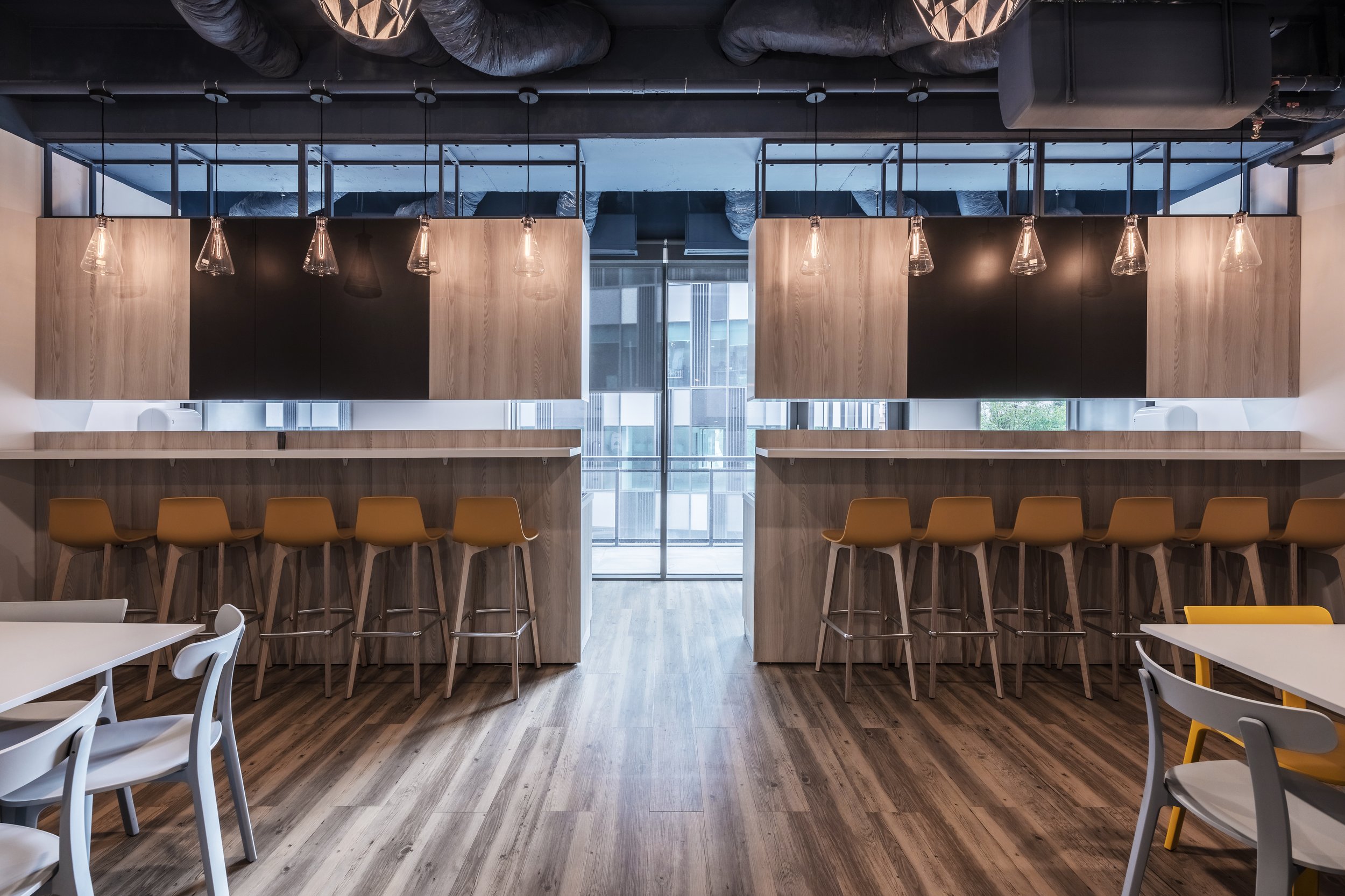 Modern breakfast bar area with six tan bar stools lined up at the counter, overhead pendant lights, and large windows with a city view.
