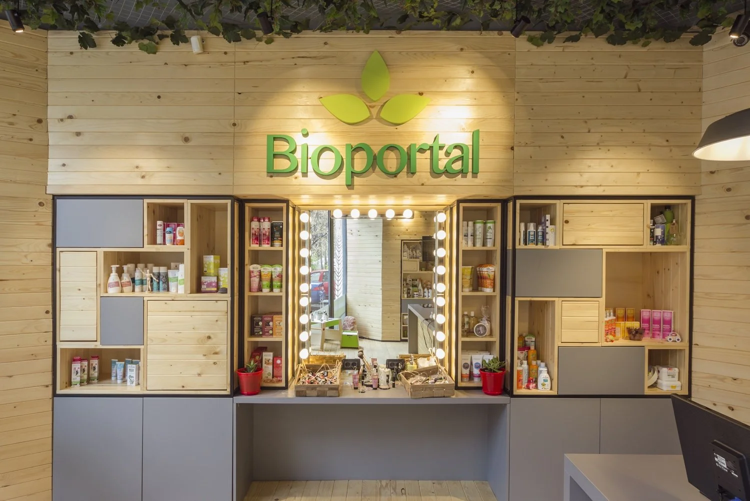 Interior of a store named Bioprotal with wooden shelves stocked with skincare products, a mirror framed with lights, and the store's logo with a leaf design above.