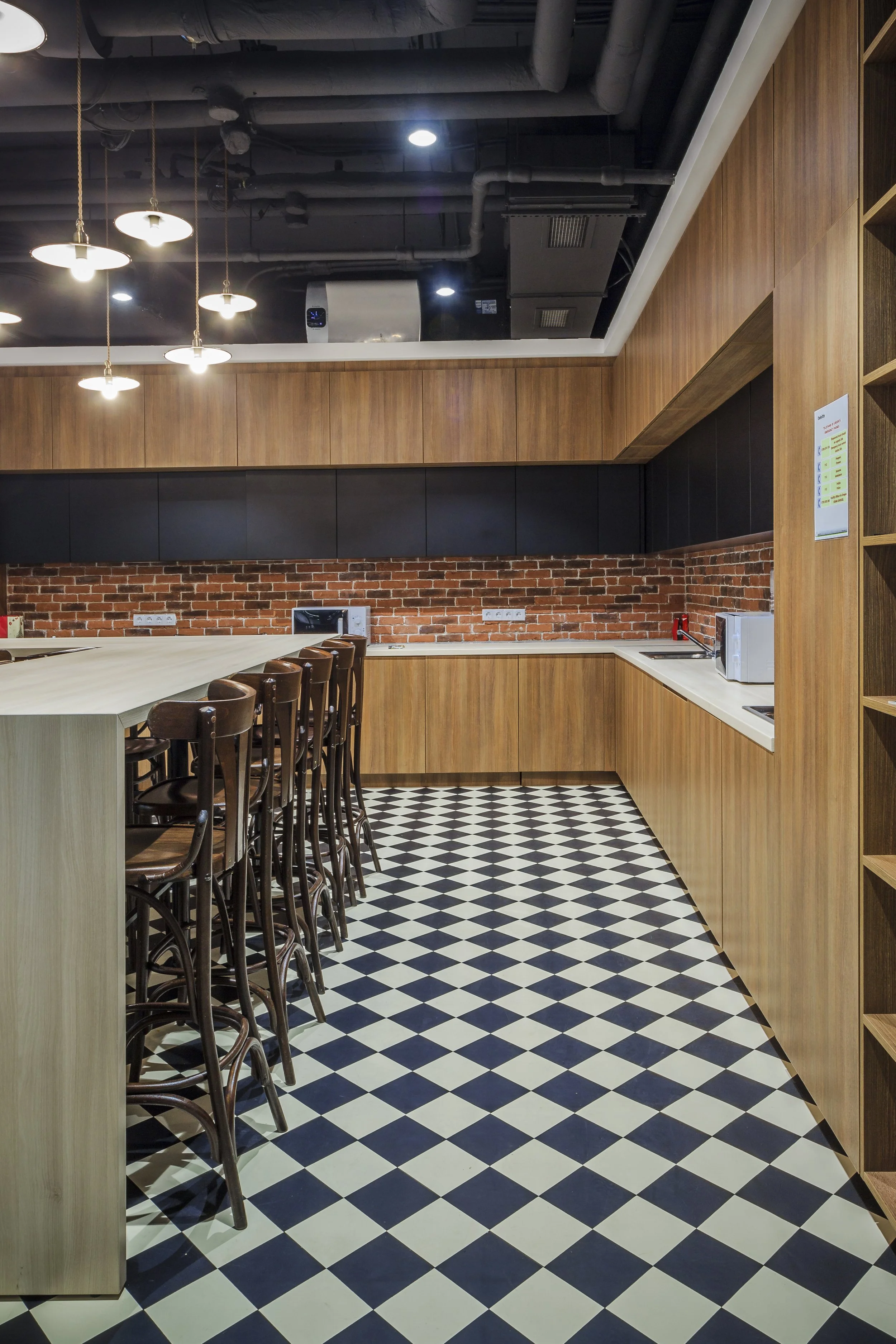Modern kitchen with wood cabinets, black upper cabinets, brick backsplash, checkered floor, and bar seating area with high chairs.
