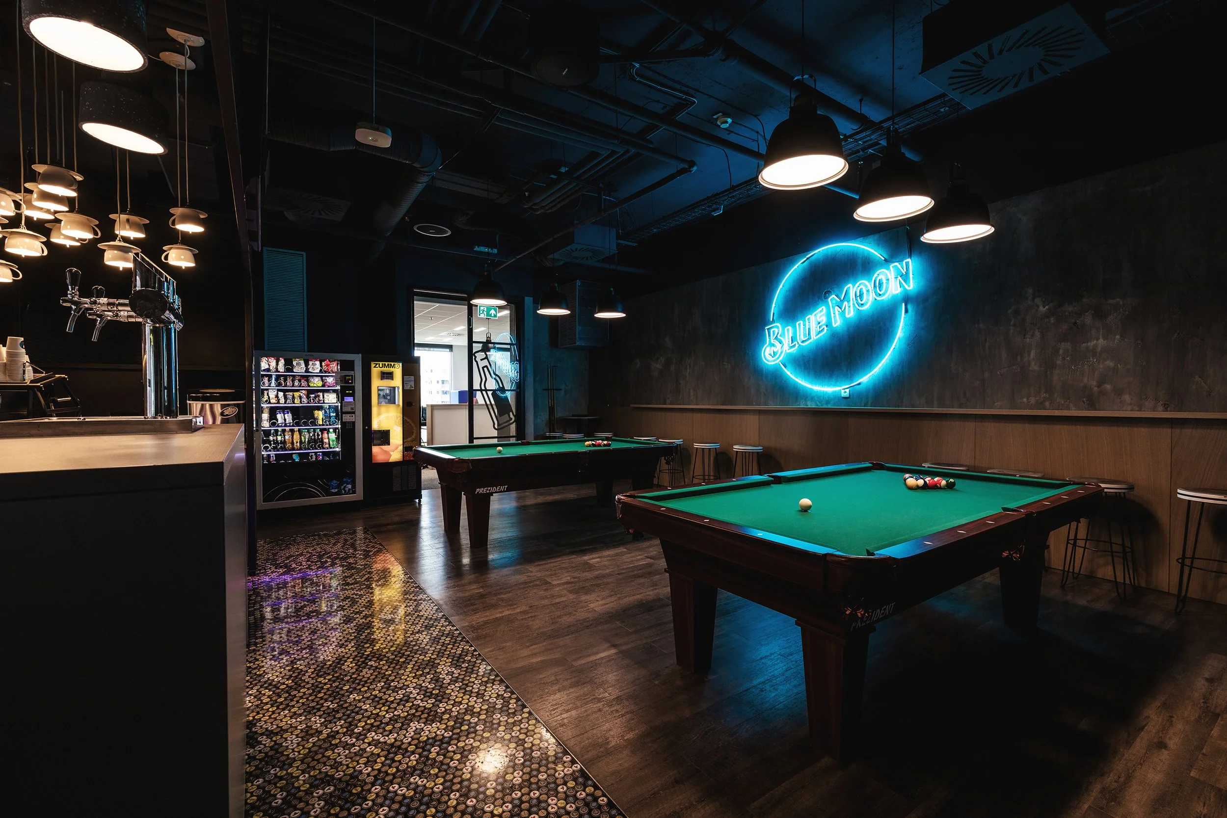Indoor bar with pool tables, neon sign reading 'Blue Moon,' vending machine, and hanging pendant lights.