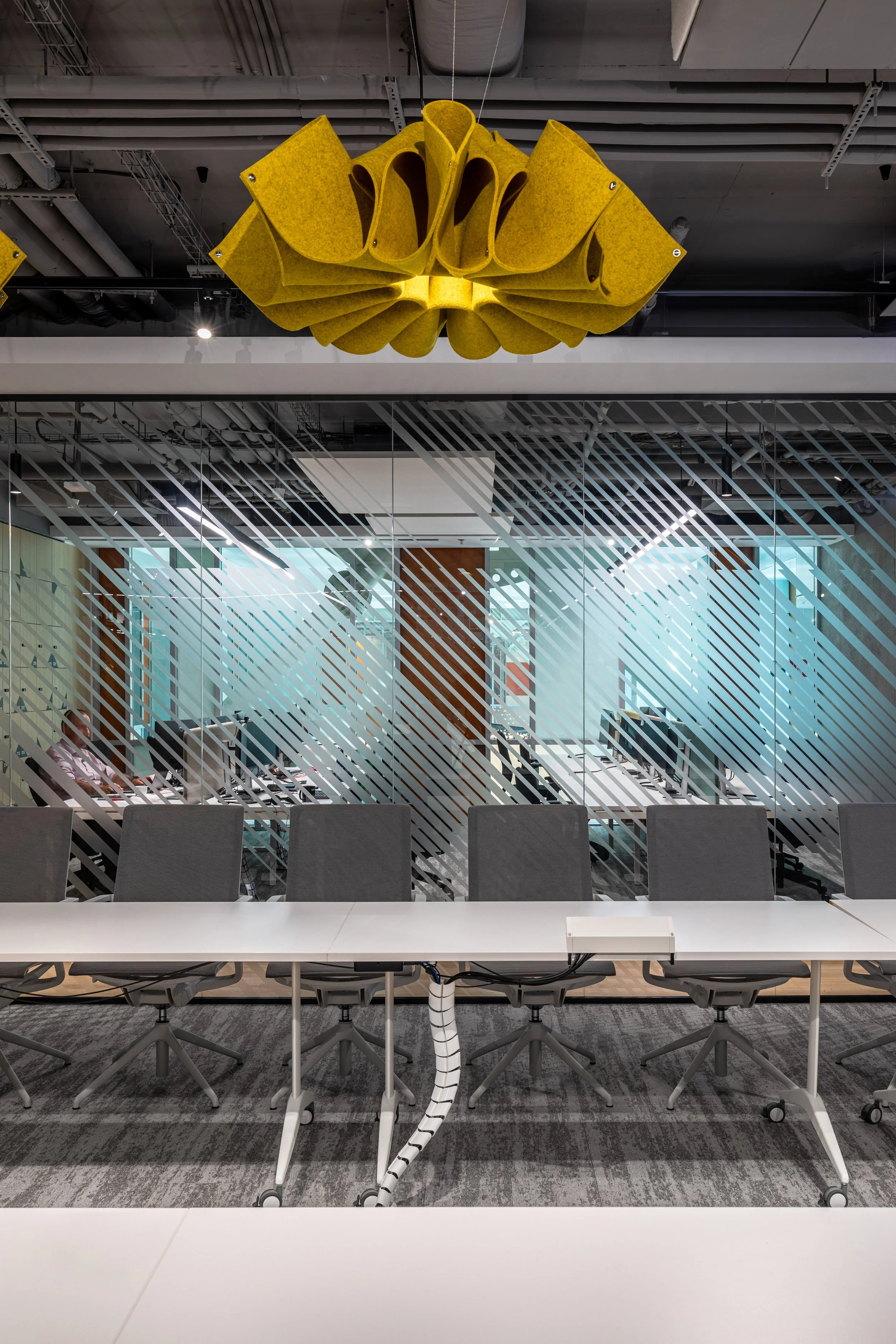 Modern conference room with a long table and chairs in front of glass walls, with yellow acoustic panels hanging from the ceiling.