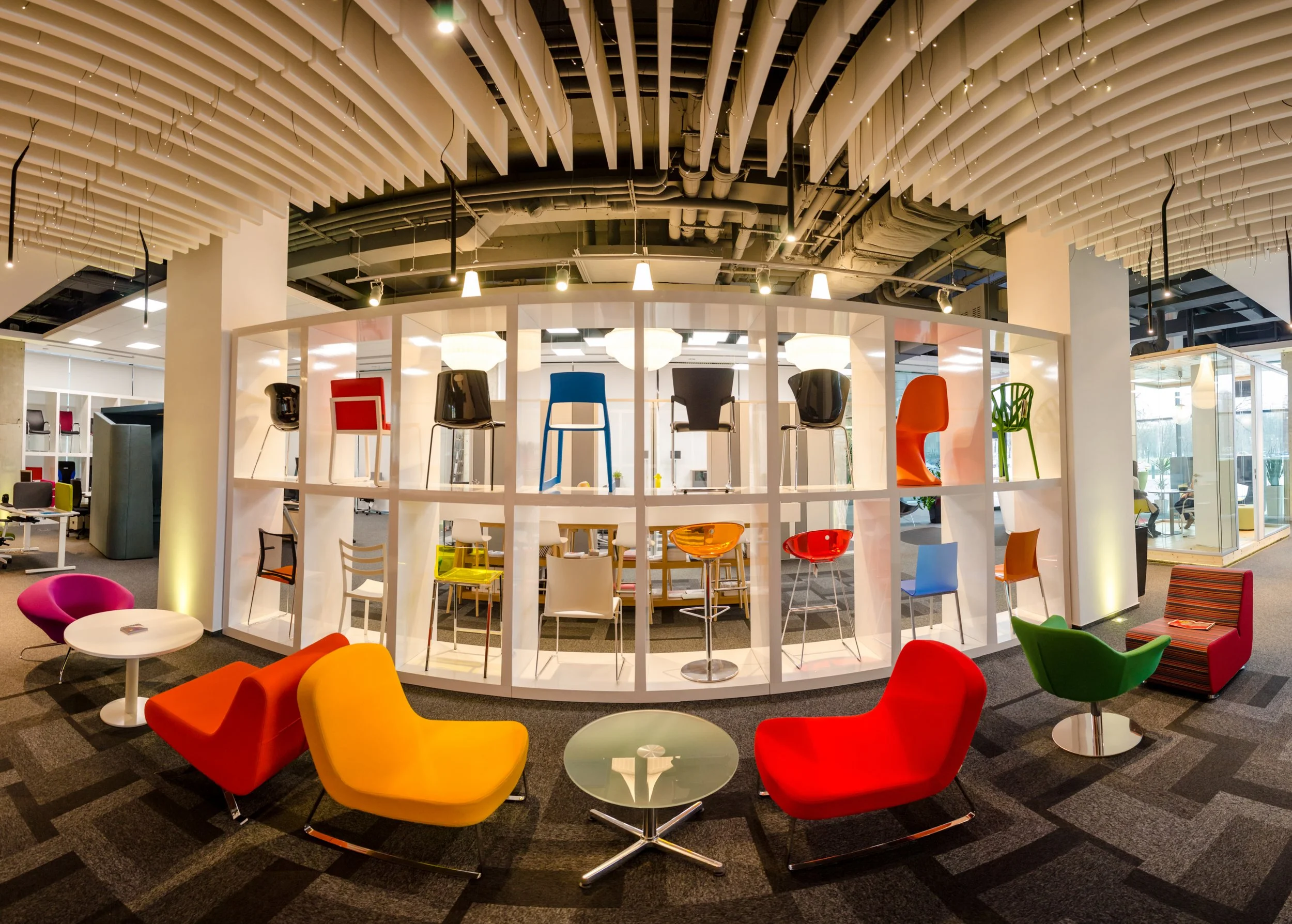 Colorful chairs and tables in a modern office lounge area with unique ceiling design.