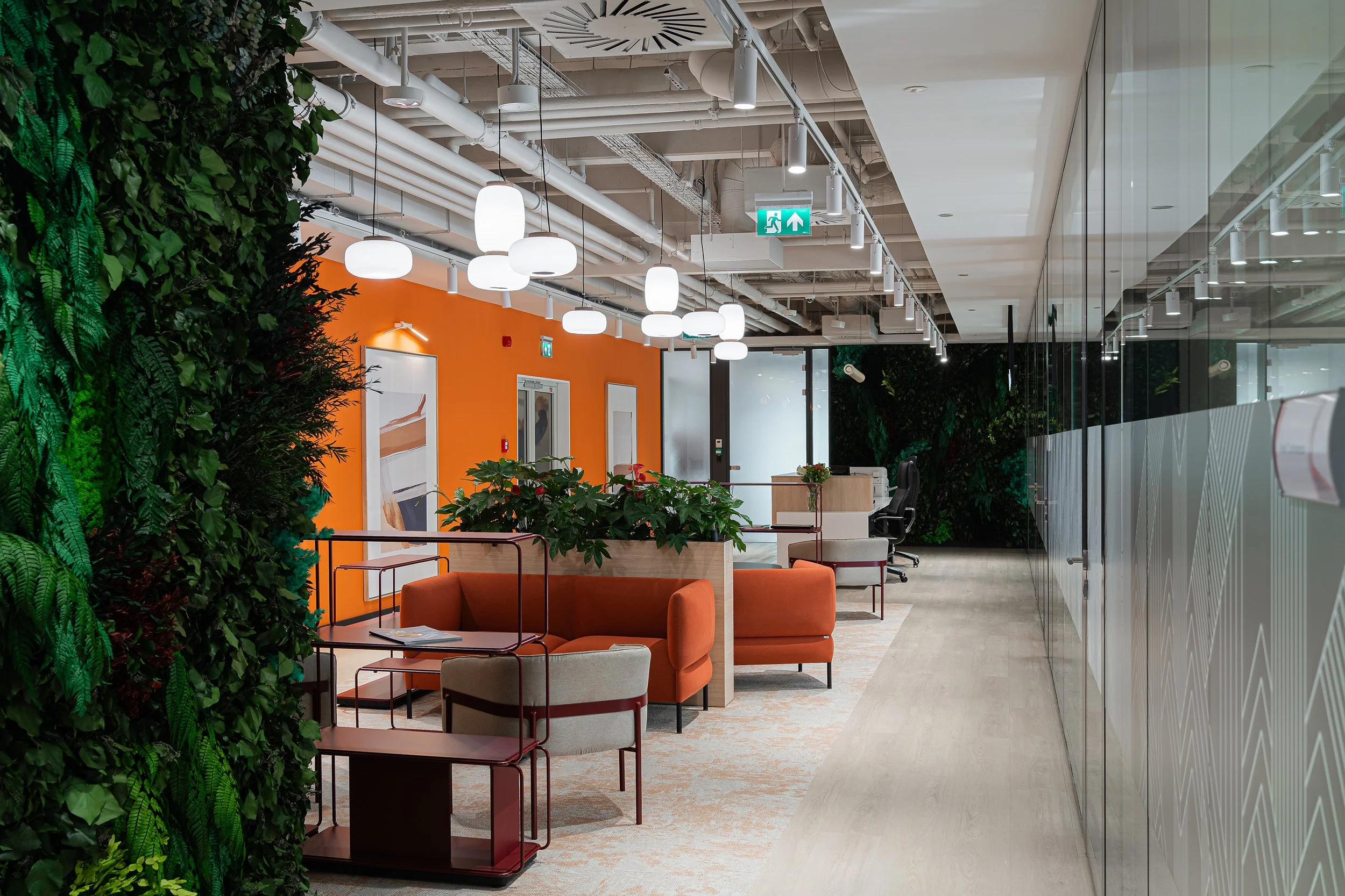 Modern office reception area with orange wall, indoor plants, seating, and a glass wall.