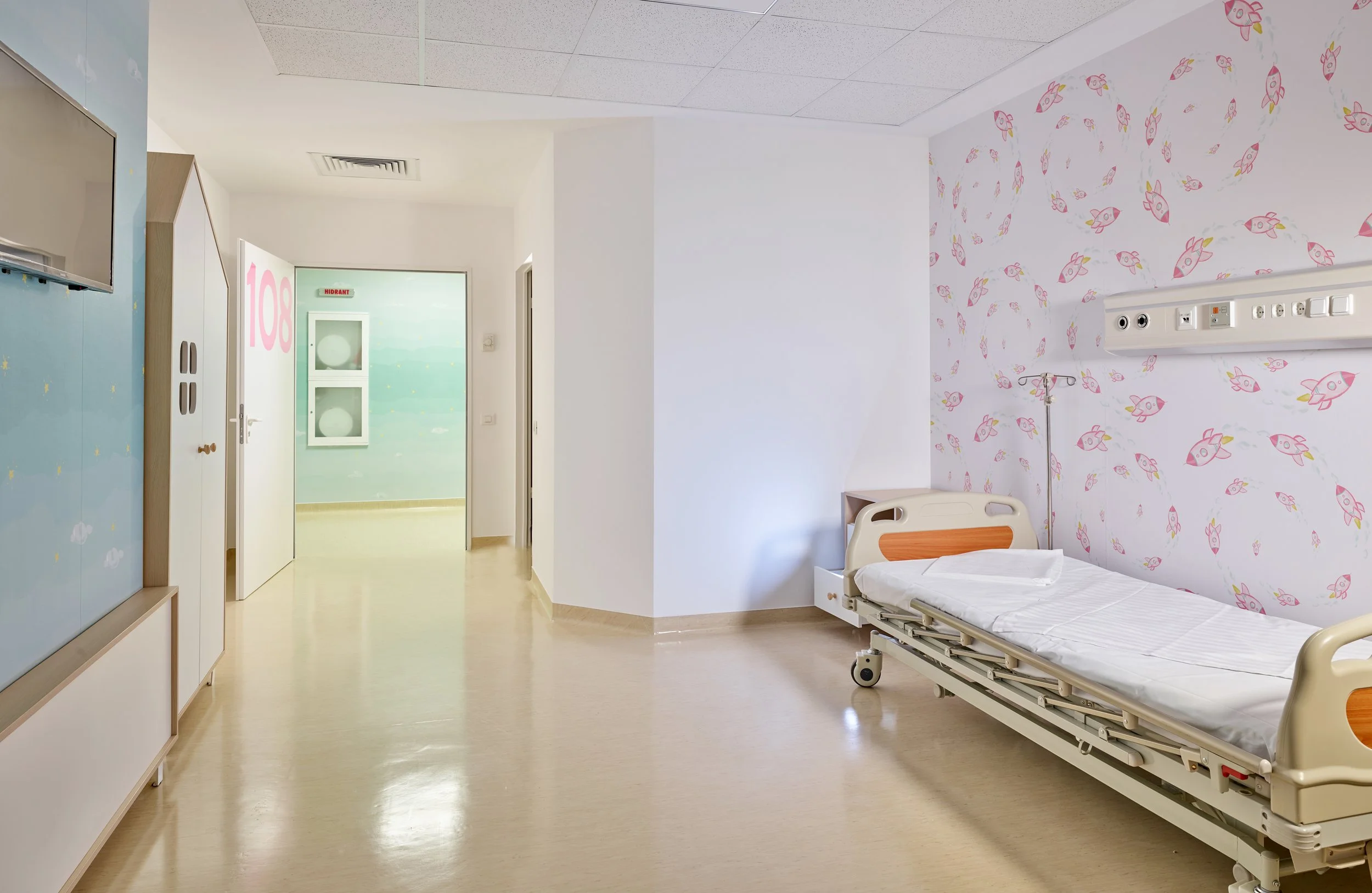 Empty hospital room with a bed, patterned wall, and hospital equipment.