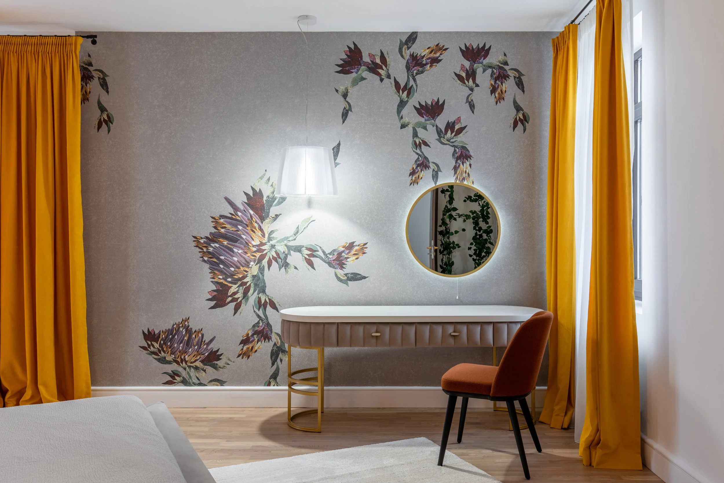 Interior of a room with a patterned wall, yellow curtains, a white desk, a round mirror, and a brown chair.