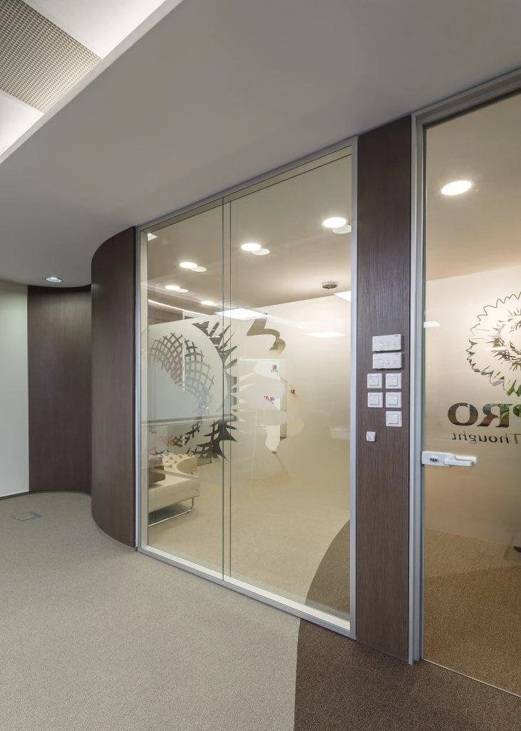 Interior office space with glass walls, wood trim, and a seating area visible through frosted glass with a logo.